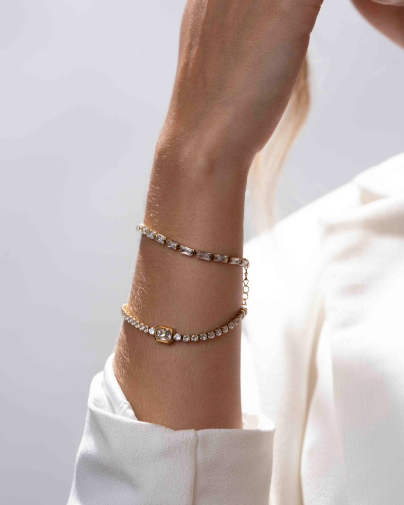 Close-up of a wrist wearing two gold bracelets on a light background