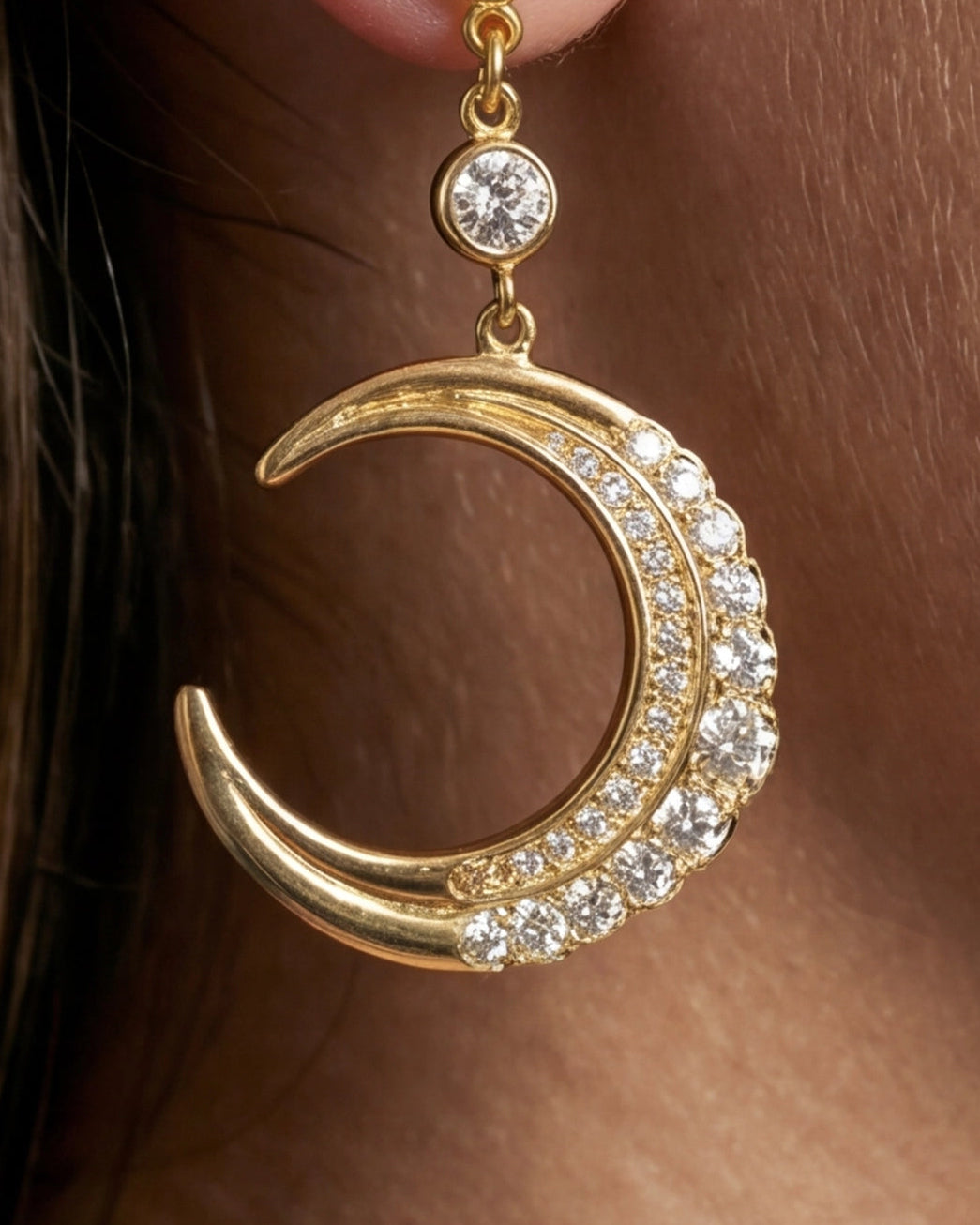 Gold crescent moon earring with clear stones on a person's ear.