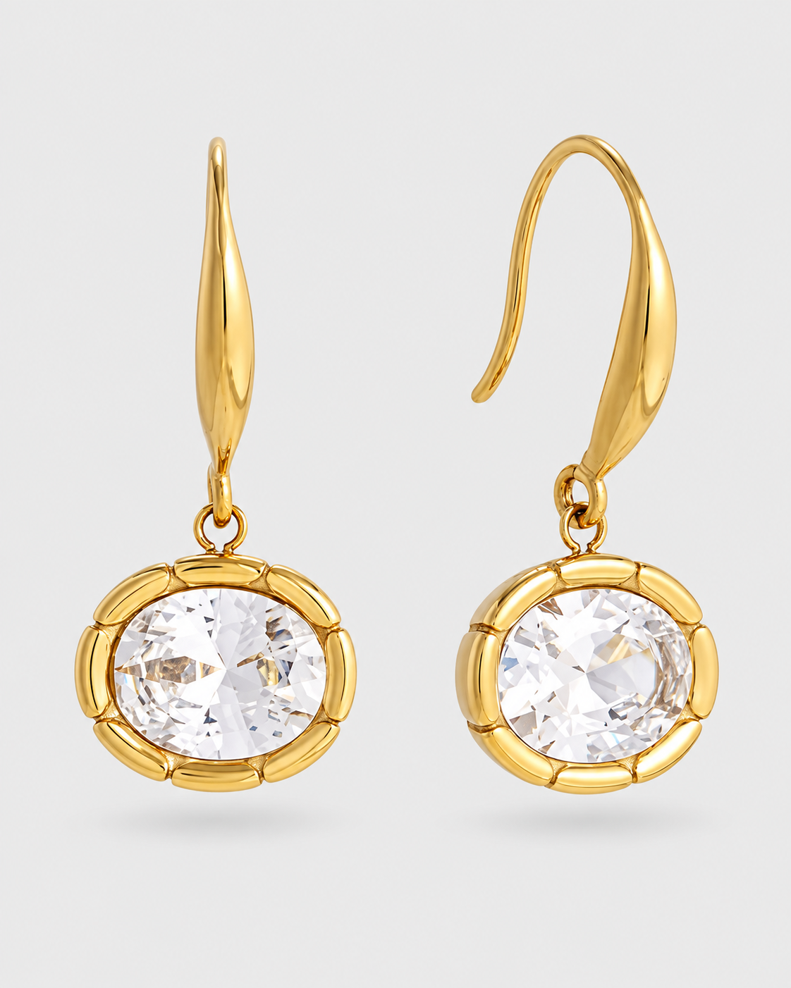 A pair of gold drop earrings with teardrop-shaped hooks and round bezel-set clear gemstones, shown on a light gray background.