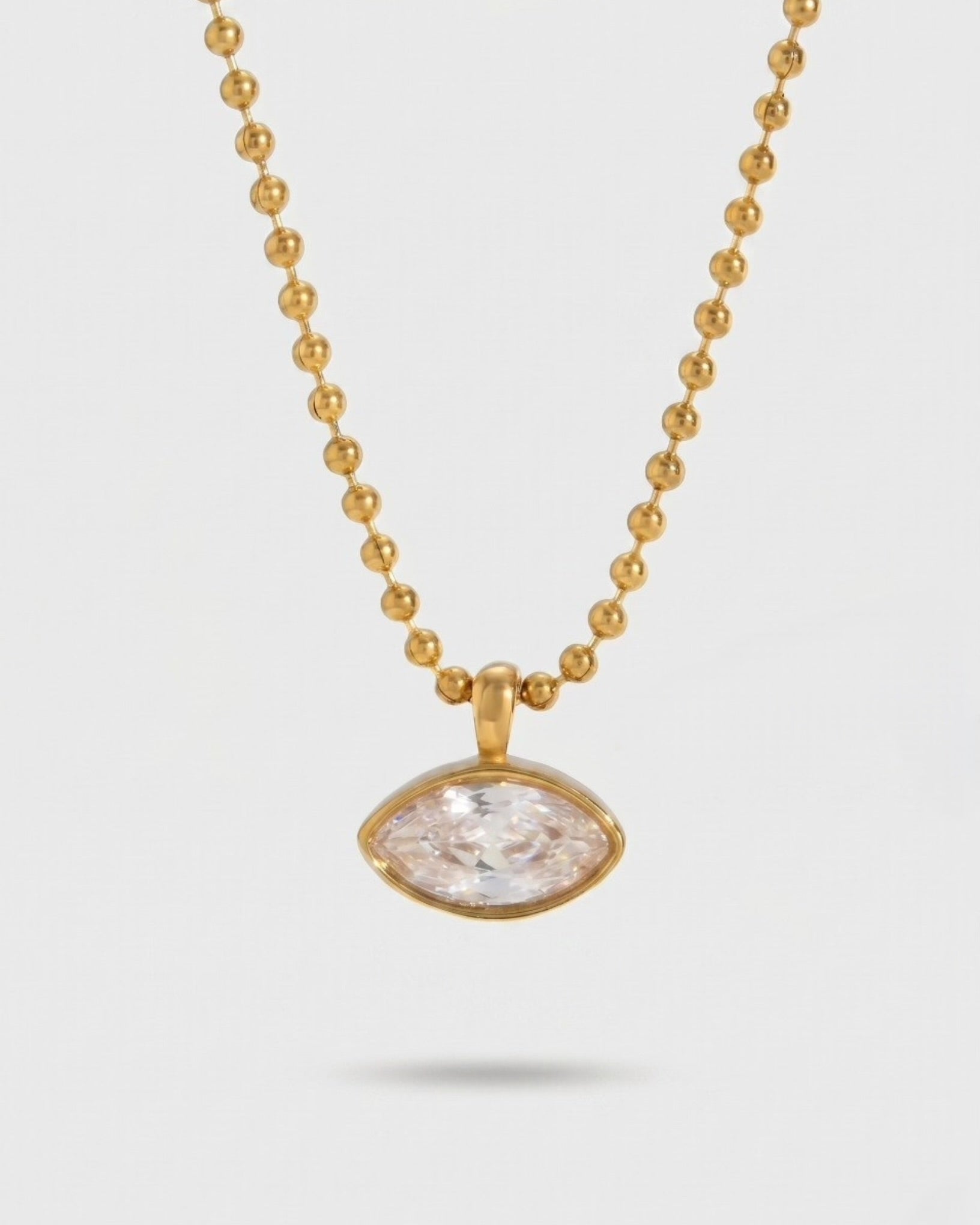 Gold necklace with a clear stone pendant on a light gray background