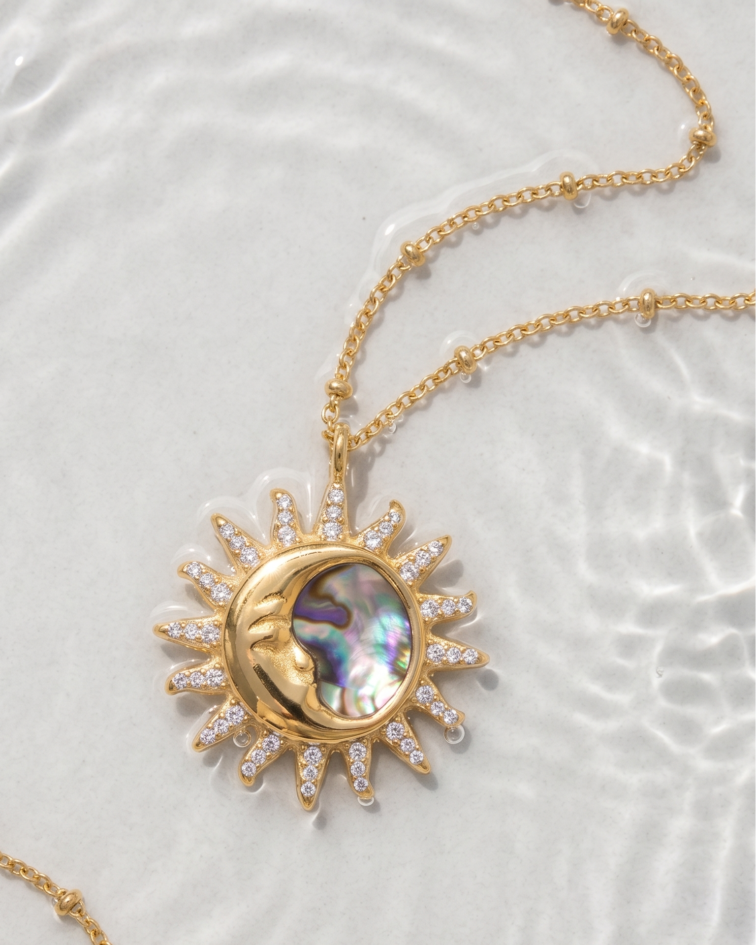 Gold necklace with a sun and moon pendant on a textured white background