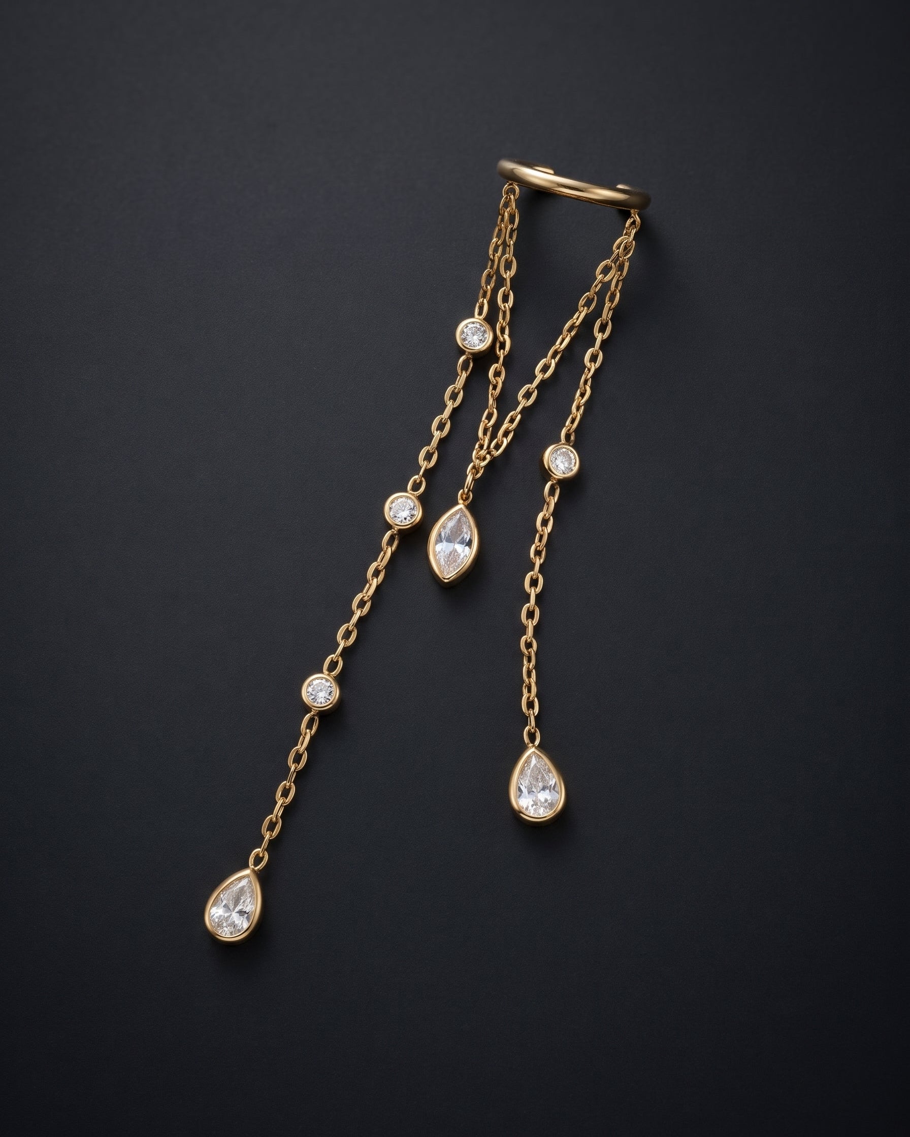 A gold chain body jewelry piece with three dangling chains, each featuring a teardrop-shaped clear gemstone and several small round clear gemstones, displayed on a dark background.
