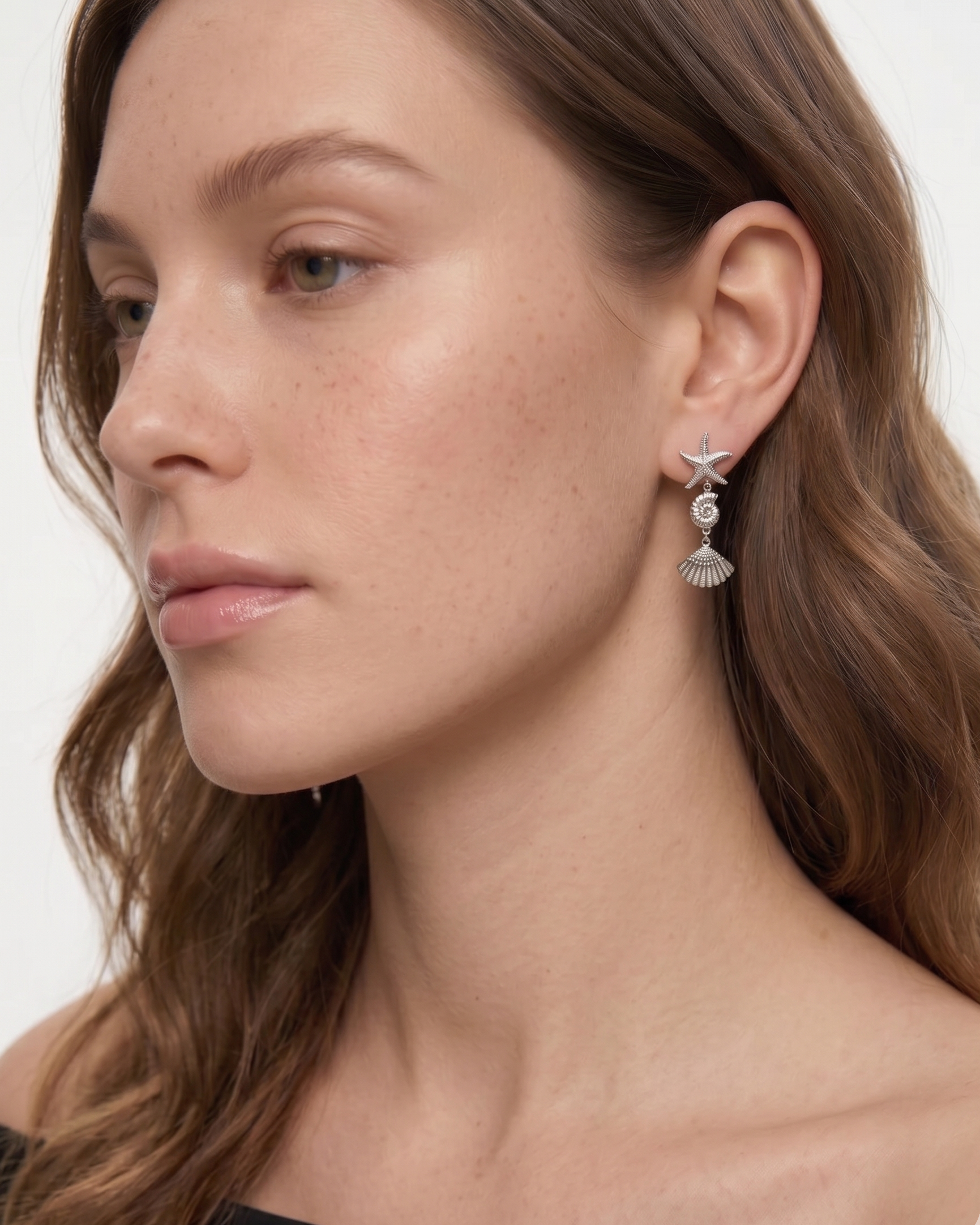 Close-up of a woman wearing starfish and shell earrings on a neutral background