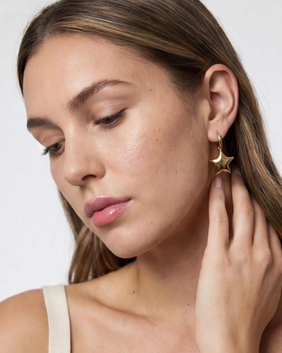 Woman wearing a gold star-shaped earring on a plain background