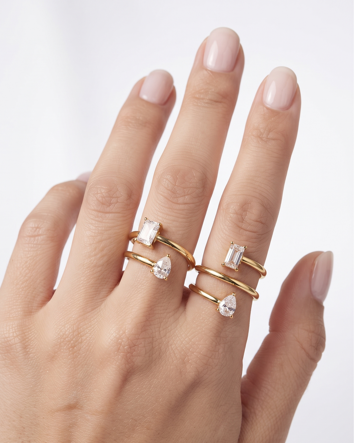 A close-up of a hand wearing three gold rings with clear gemstones, set against a clean white background.