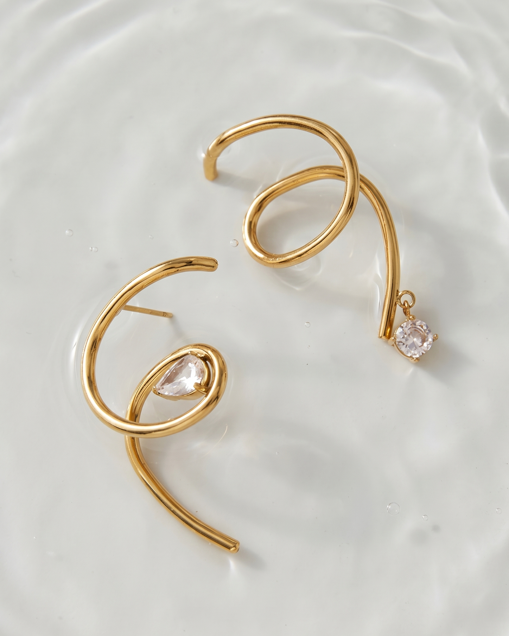 Gold hoop earrings with clear gemstones on a white plate