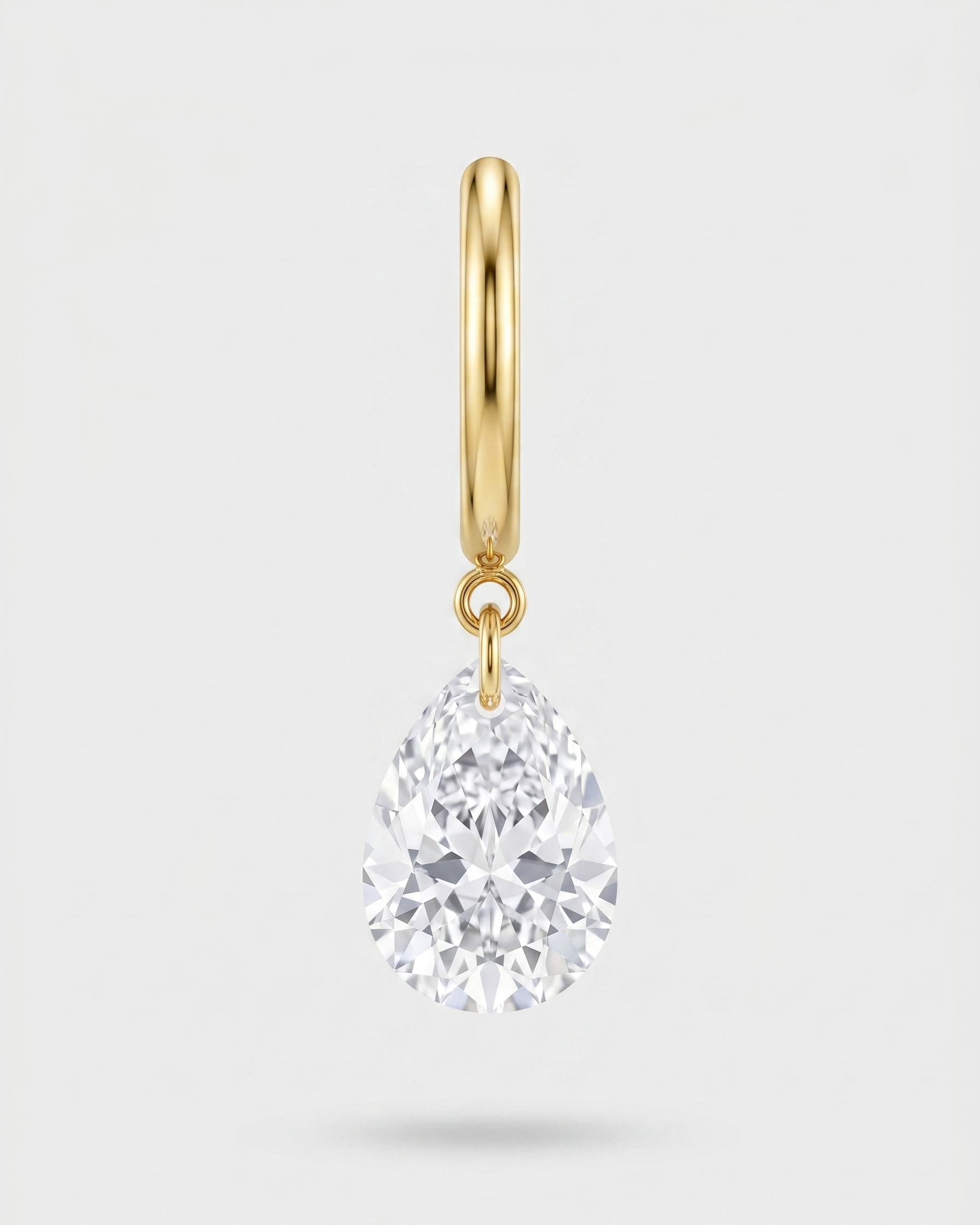 Gold earring with a teardrop-shaped diamond on a light gray background