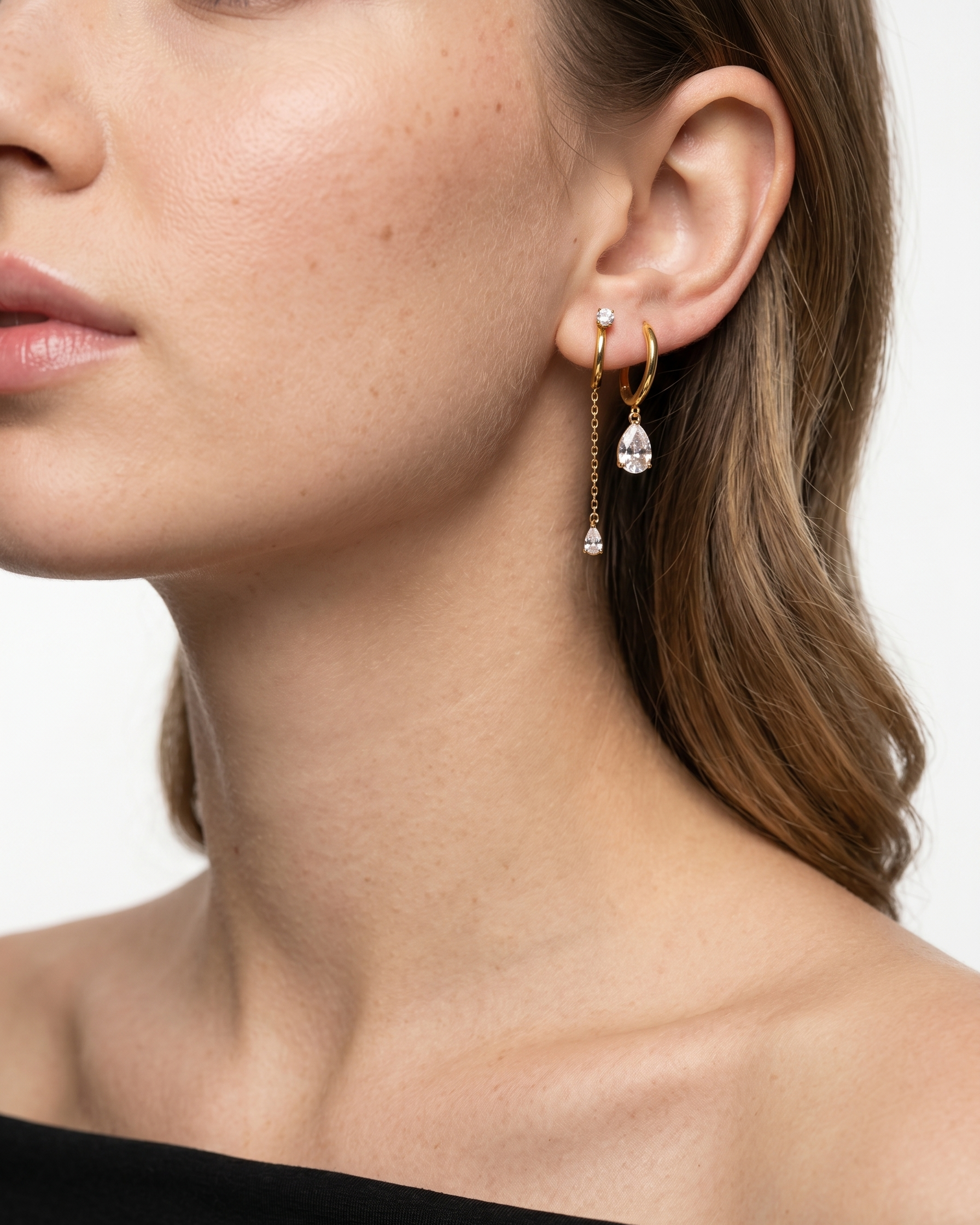 Close-up of a woman wearing gold earrings with clear gemstones on a white background