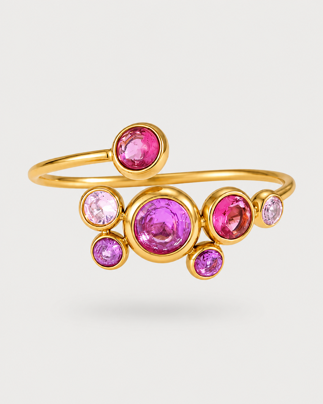 A gold-plated wrap ring featuring a cluster of round pink and purple gemstones in bezel settings, displayed on a light gray background.