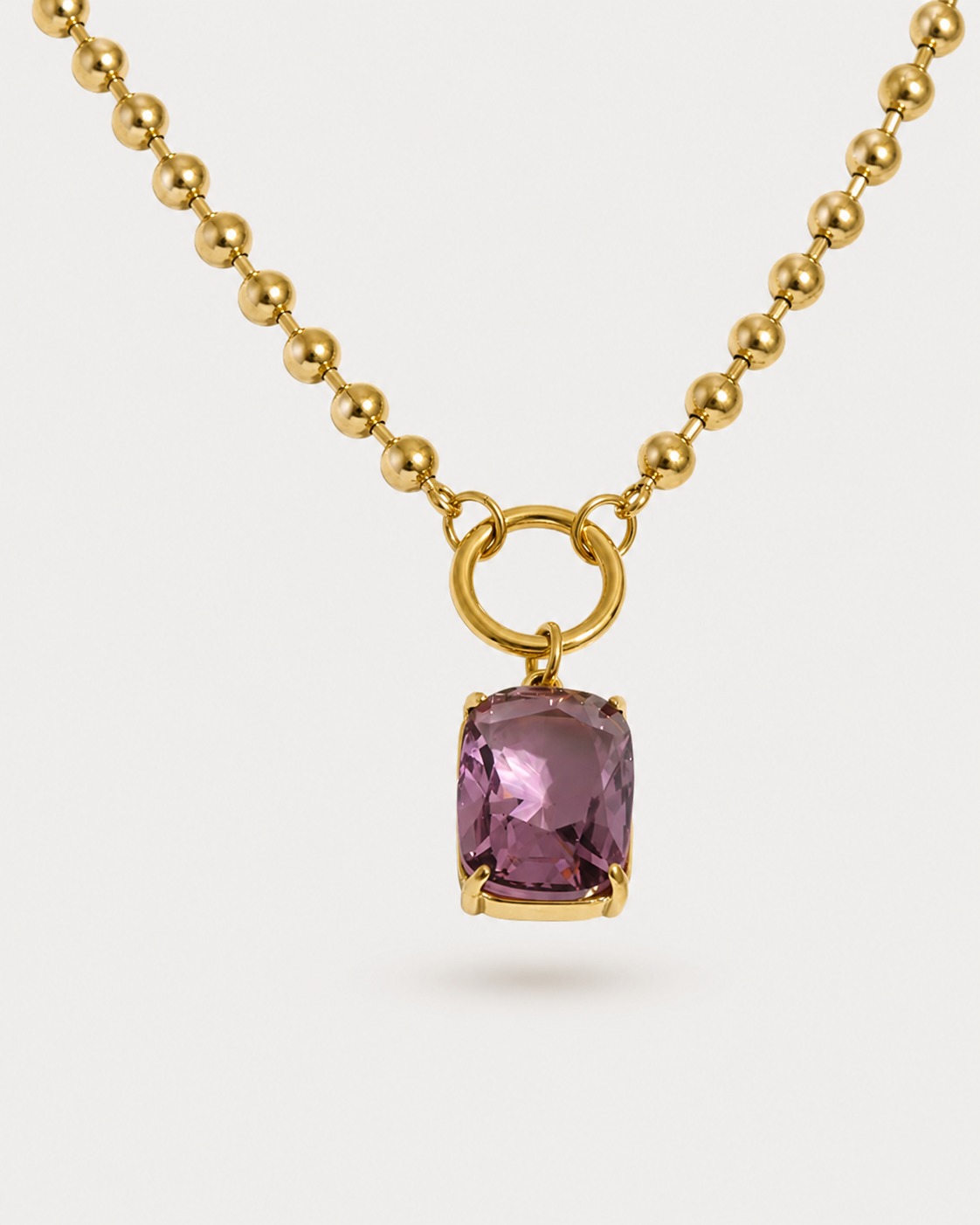 A gold ball chain necklace with a rectangular cushion-cut purple gemstone pendant, set in a gold ring clasp, shown on a light gray background.