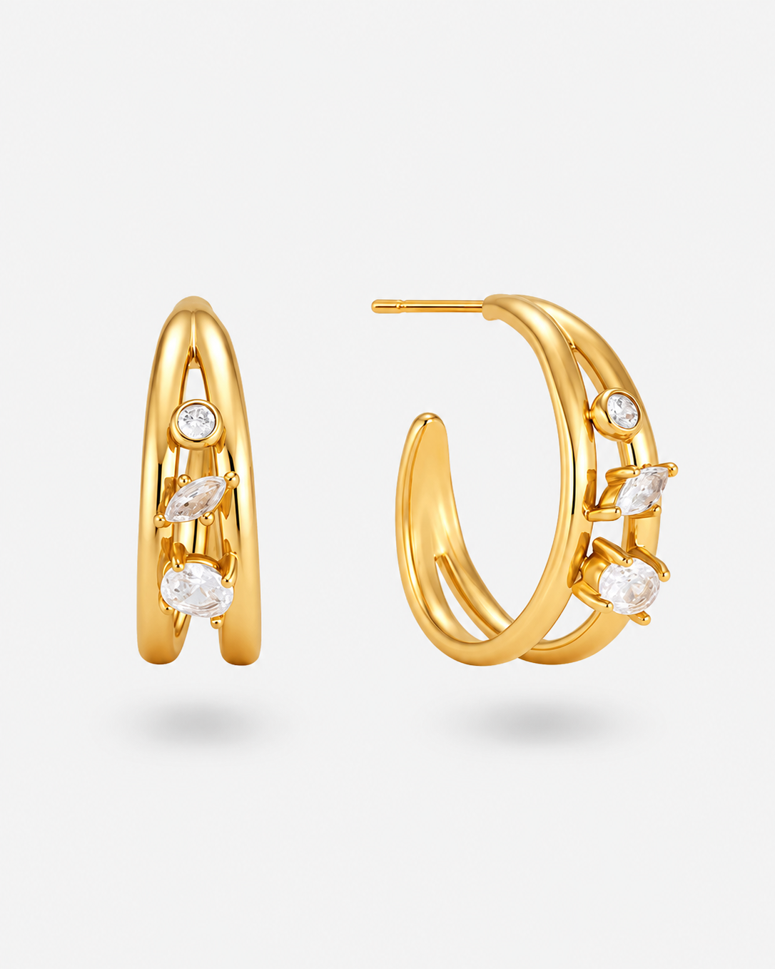 A pair of gold hoop earrings with curved, layered bands and small clear marquise and round gemstones, shown on a light gray background.