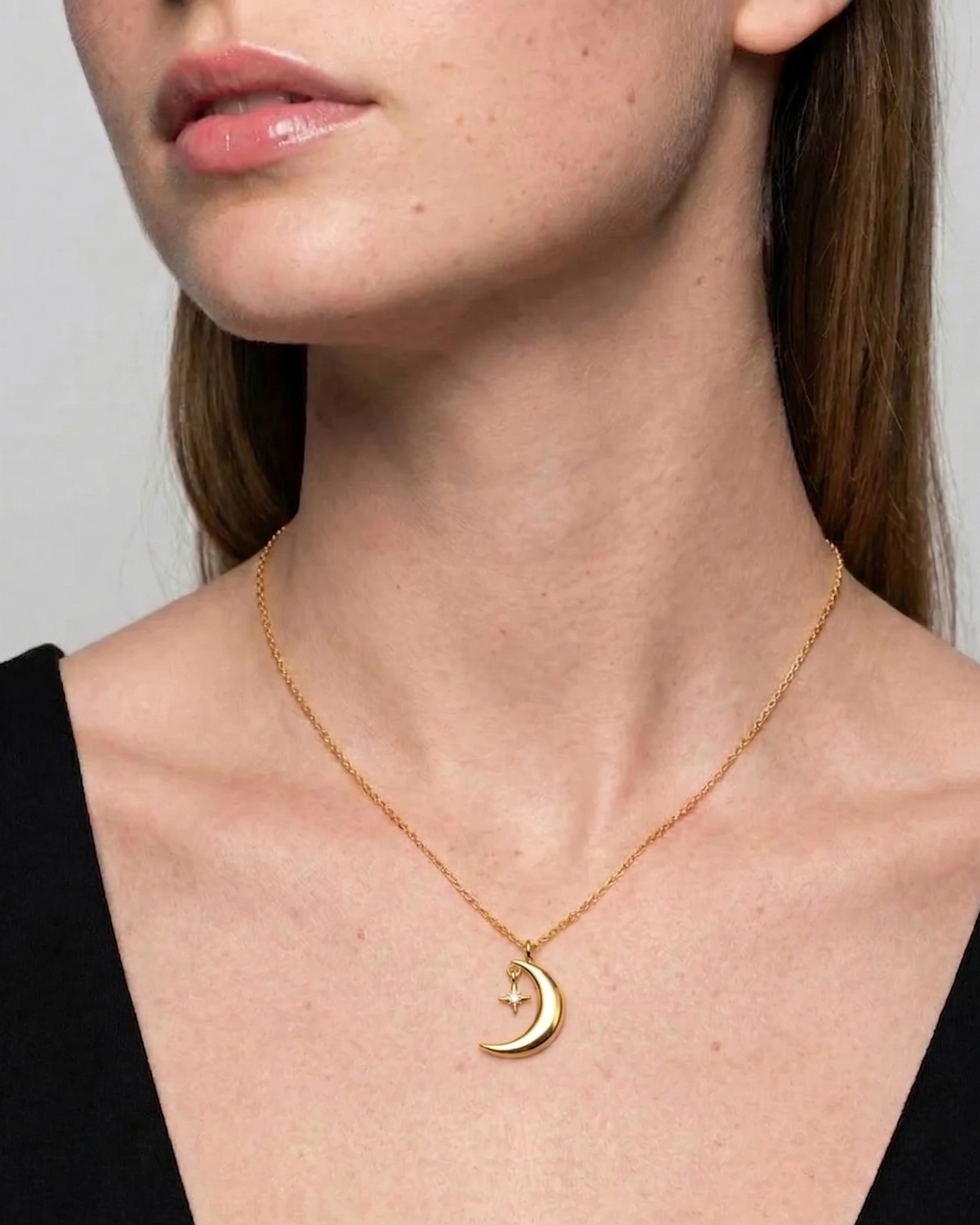 Gold necklace with a crescent moon pendant worn by a model against a neutral background