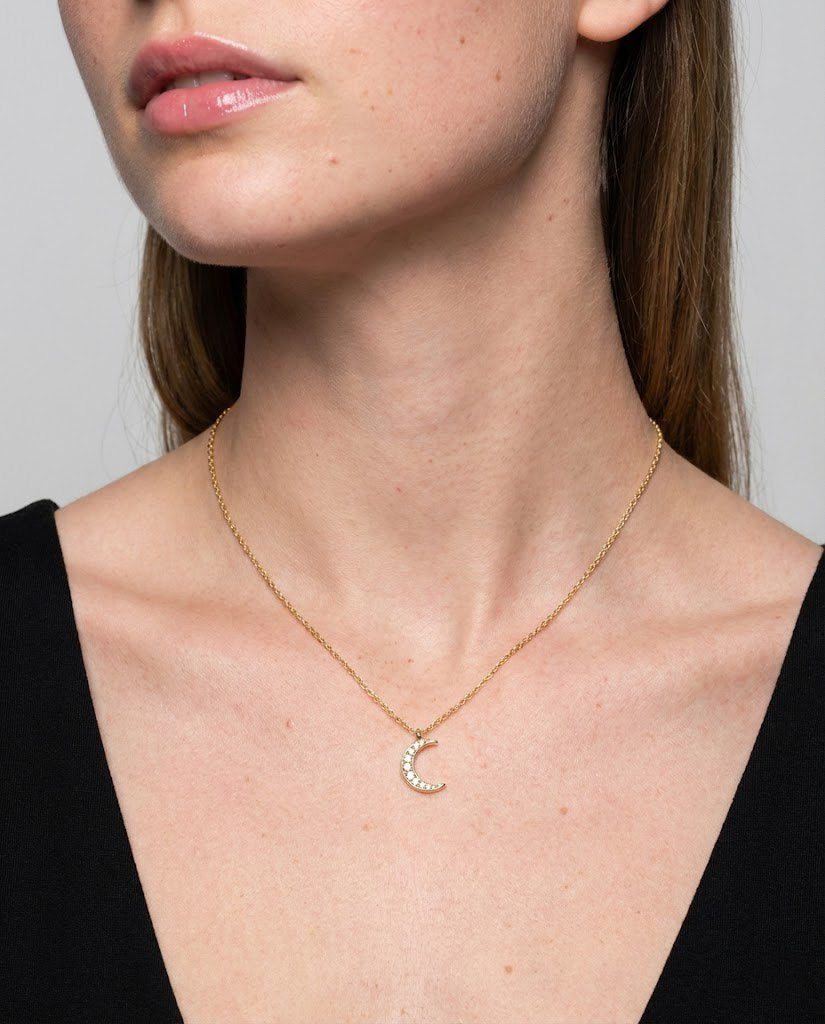 Close-up of a person wearing a gold necklace with a crescent moon pendant against a neutral background