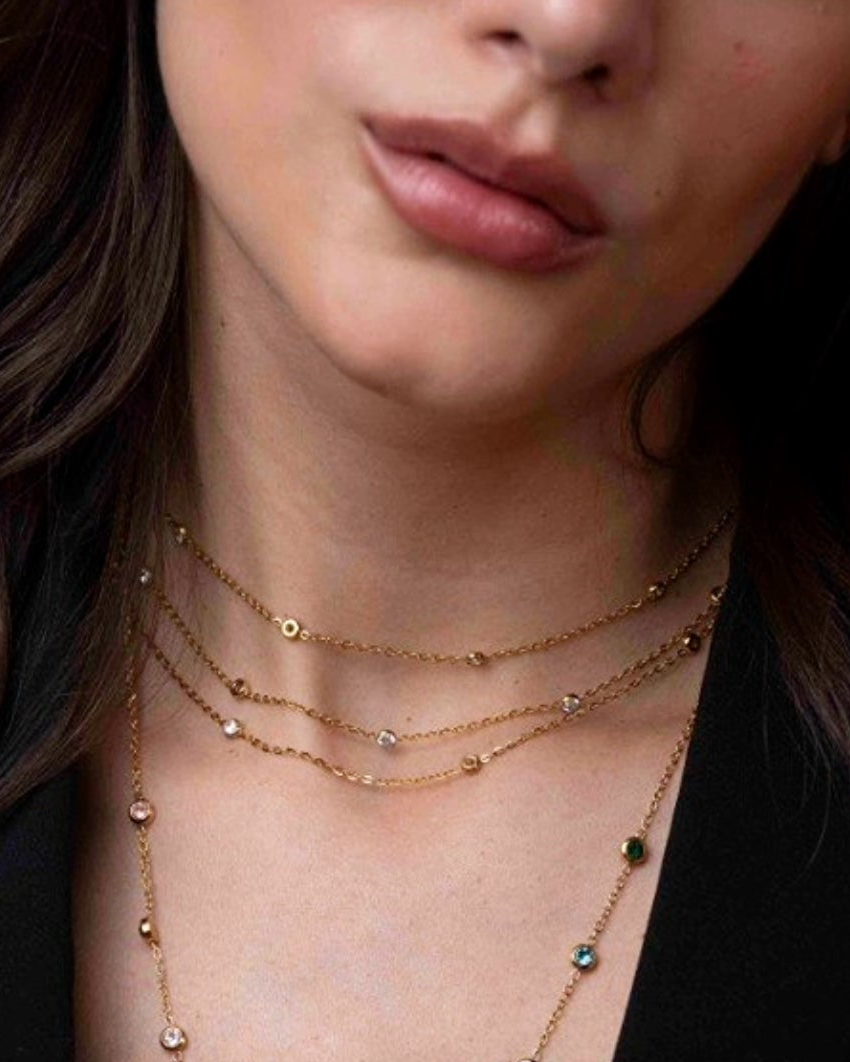 Close-up of a woman wearing multiple gold necklaces with gemstones.