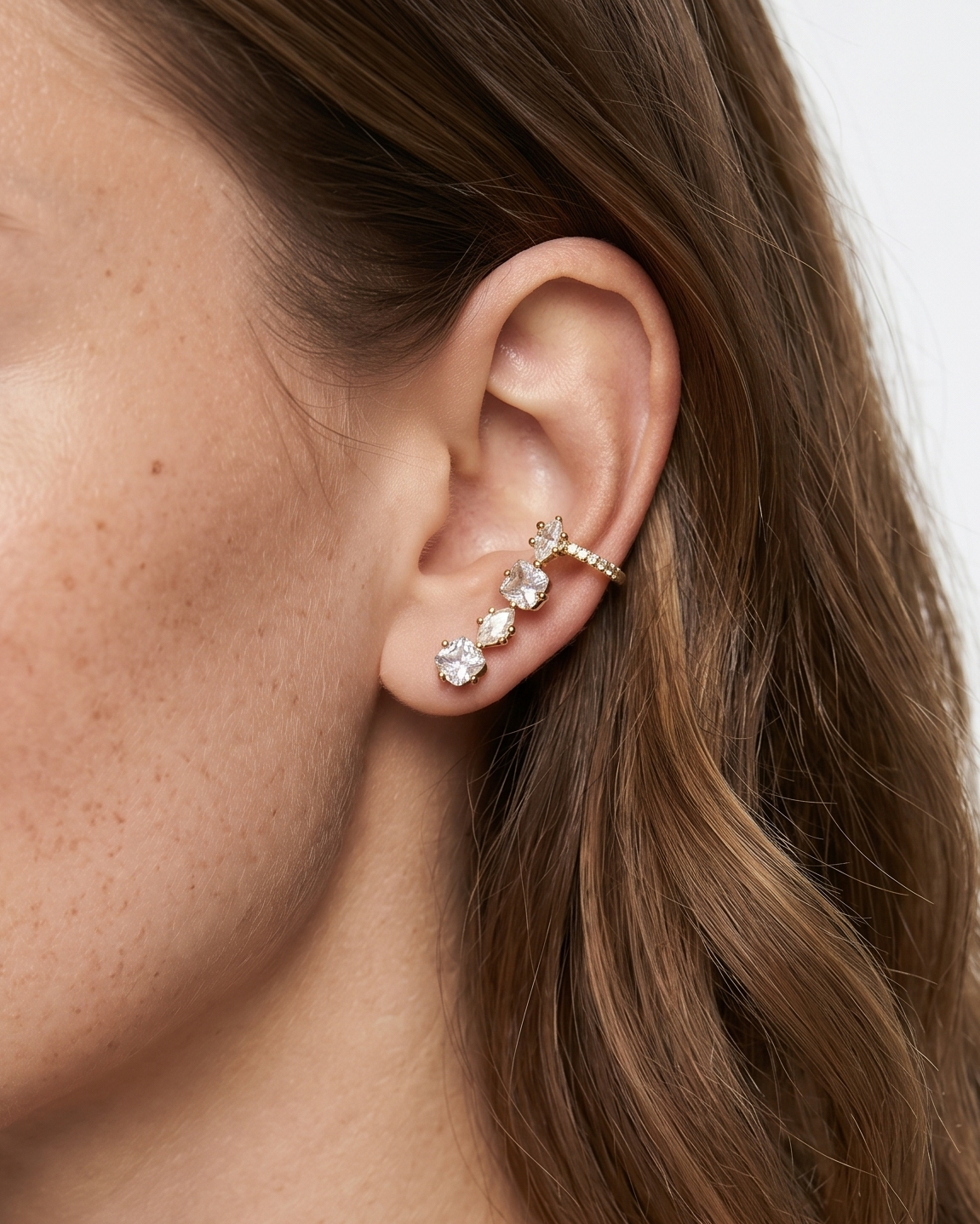 Close-up of a woman wearing a gold earring with multiple gemstones on a neutral background