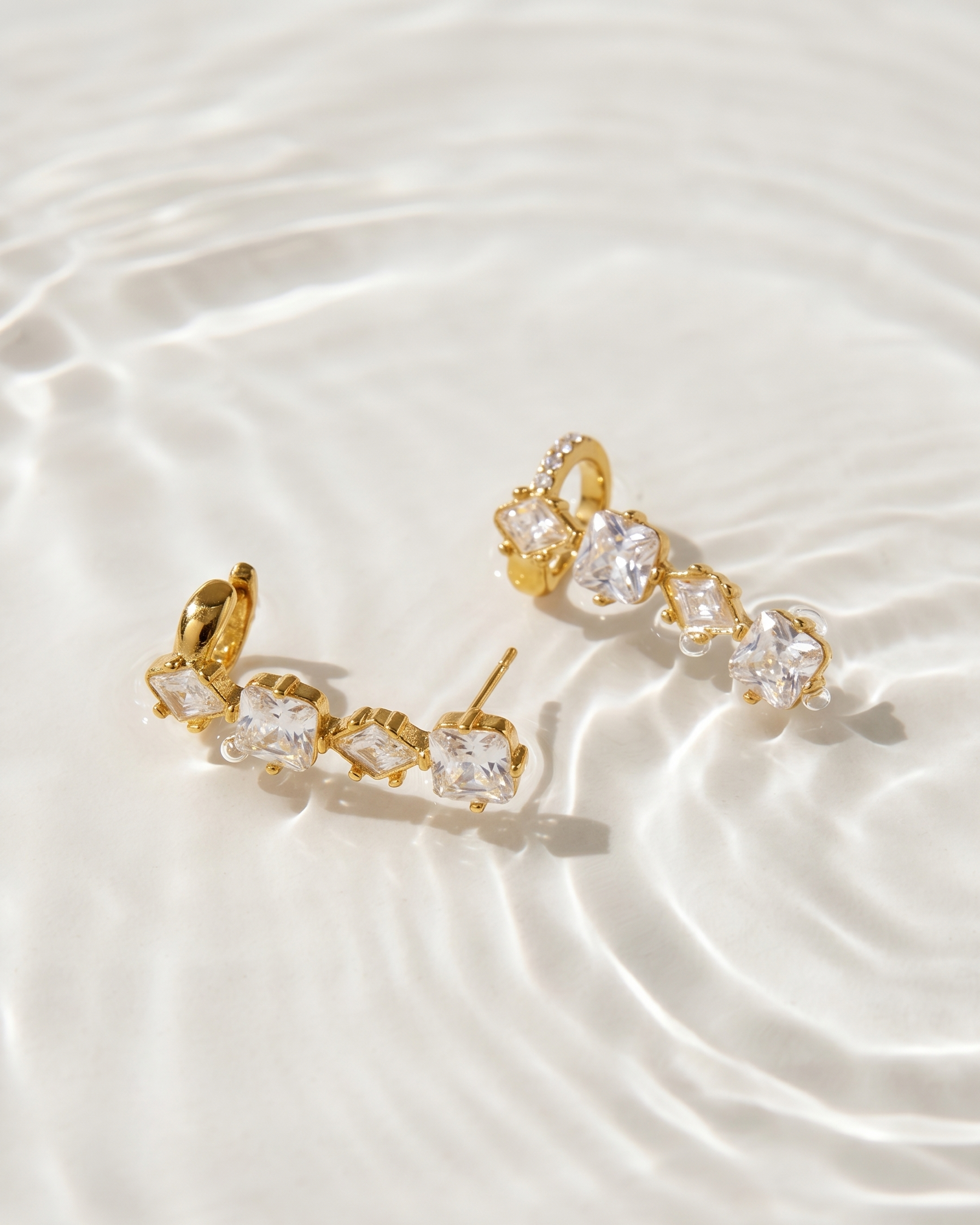 Gold earrings with clear stones on a white fabric background