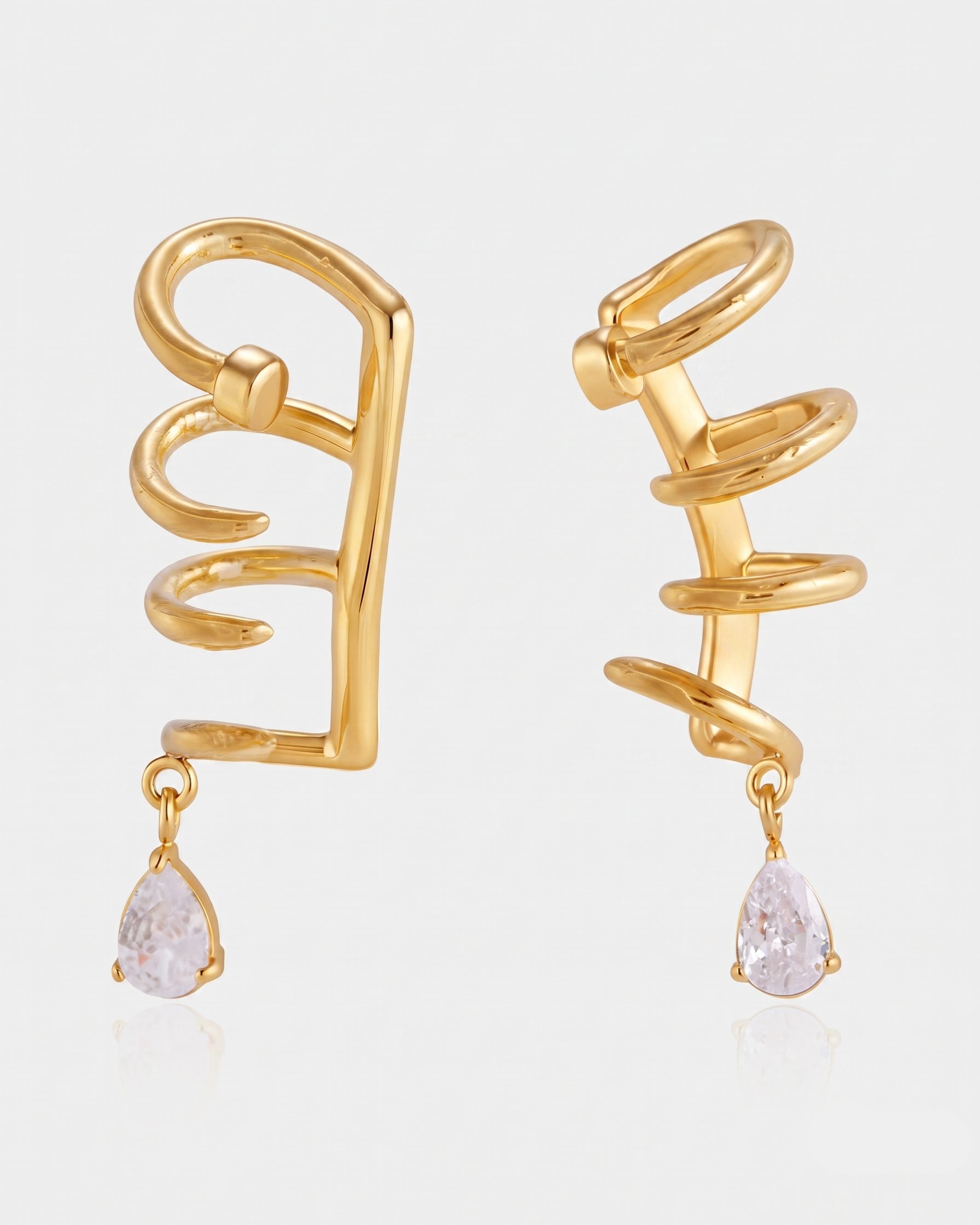 A pair of gold spiral wrap earrings with teardrop-shaped clear gemstone drops, shown on a light gray background.