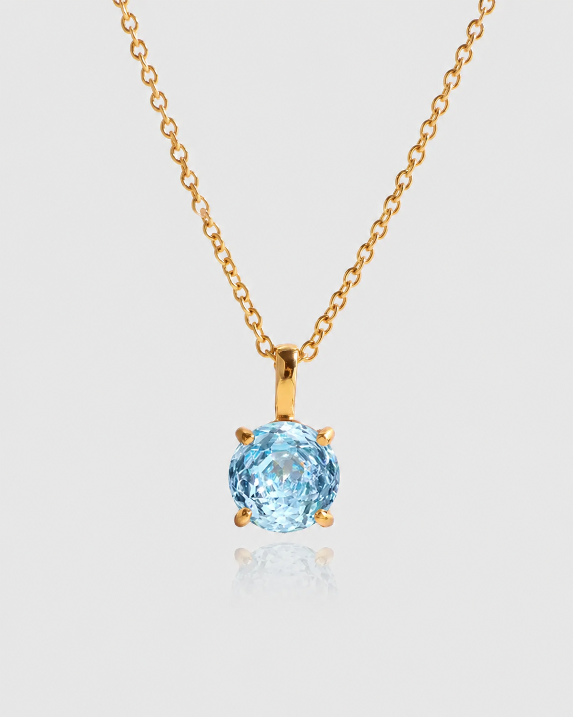 Gold necklace with a blue gemstone pendant on a light gray background