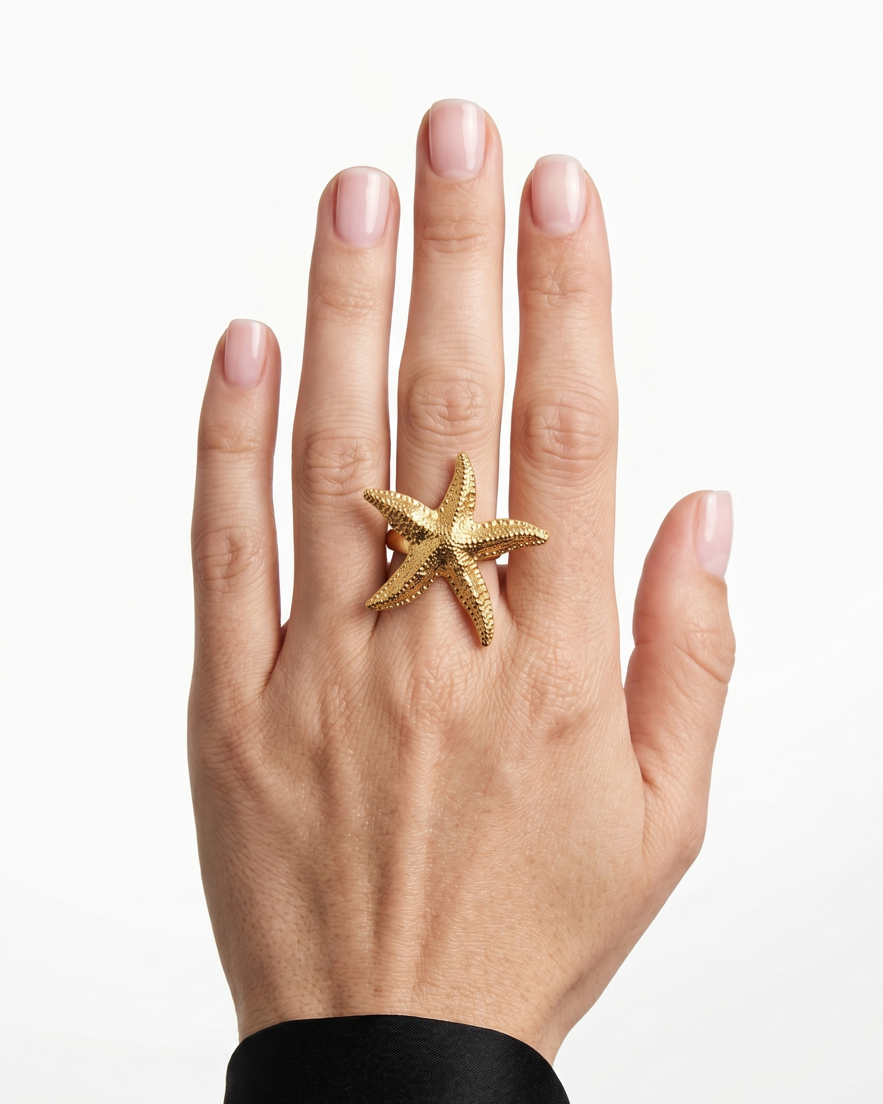 Gold starfish ring on a hand against a white background