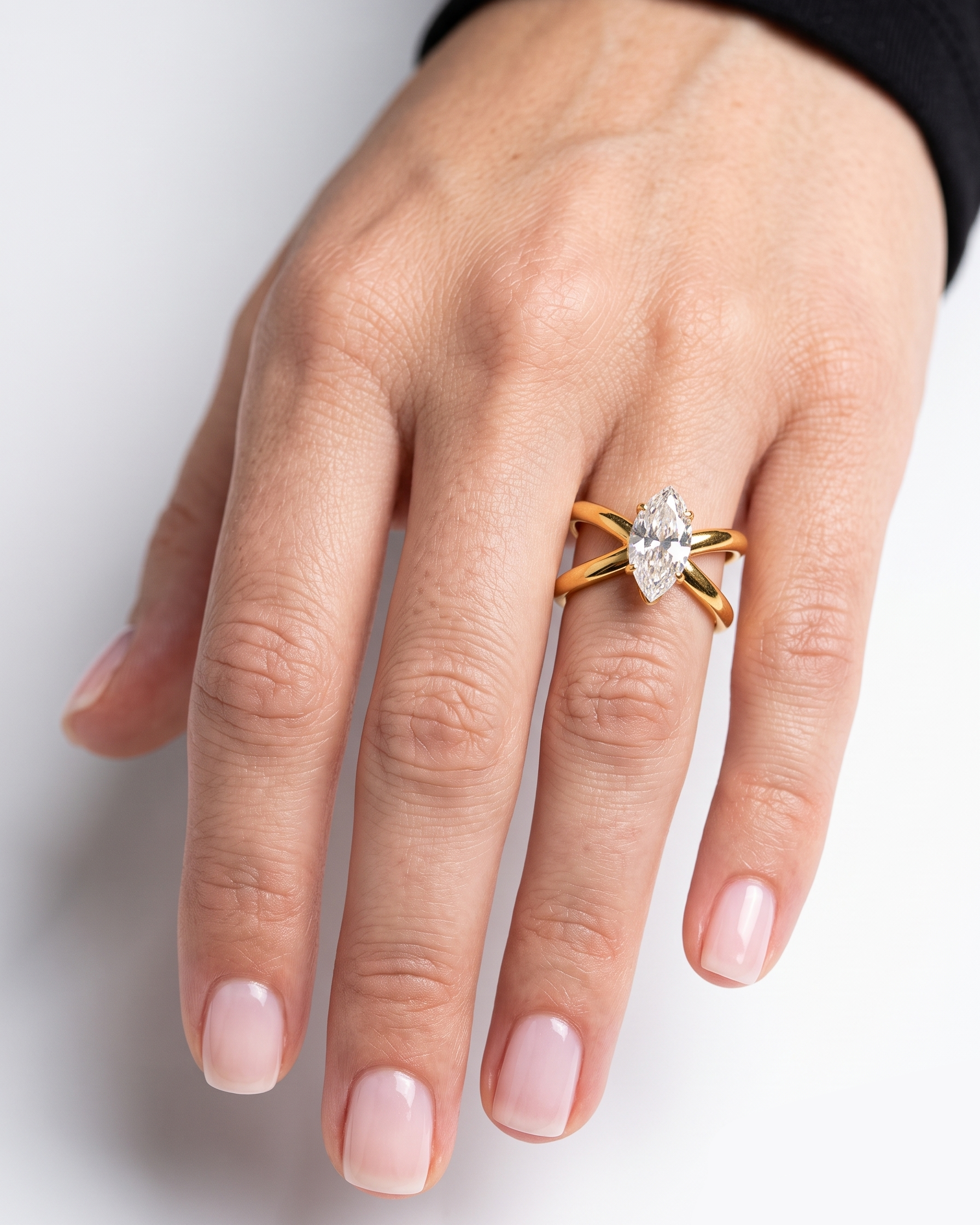 A close-up of a hand wearing a gold ring with a marquise-cut clear gemstone. The ring features a split band design with a central marquise gemstone.