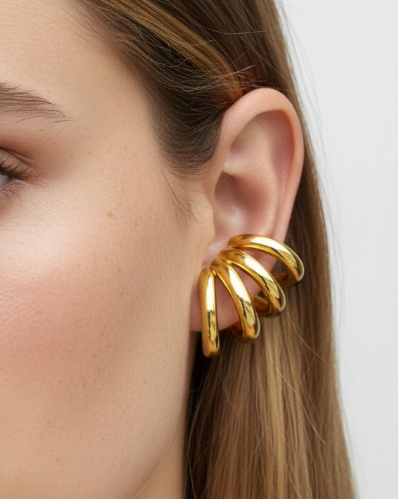 Gold spiral earring worn by a model on a plain background