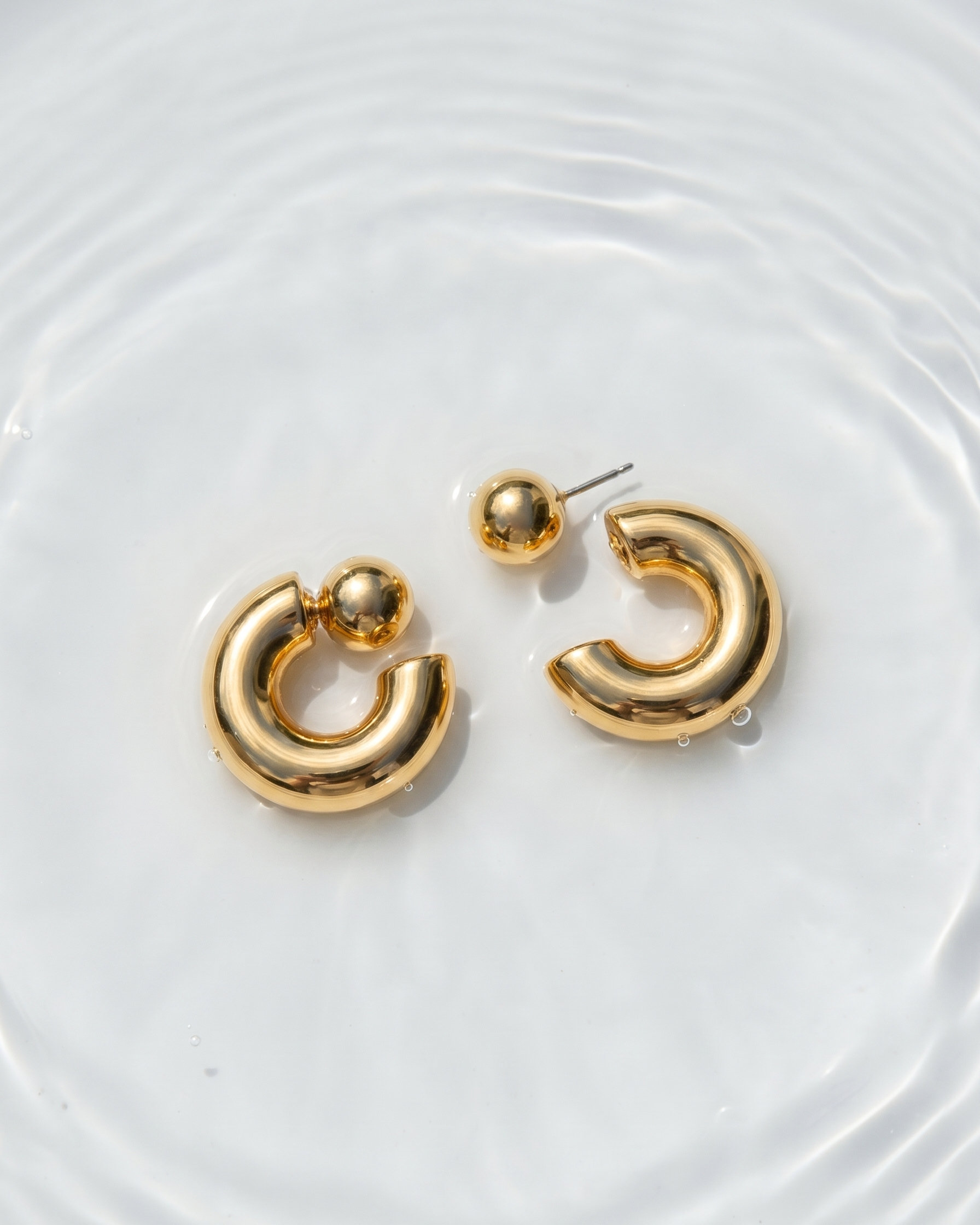 Gold hoop earrings on a white surface with water ripples