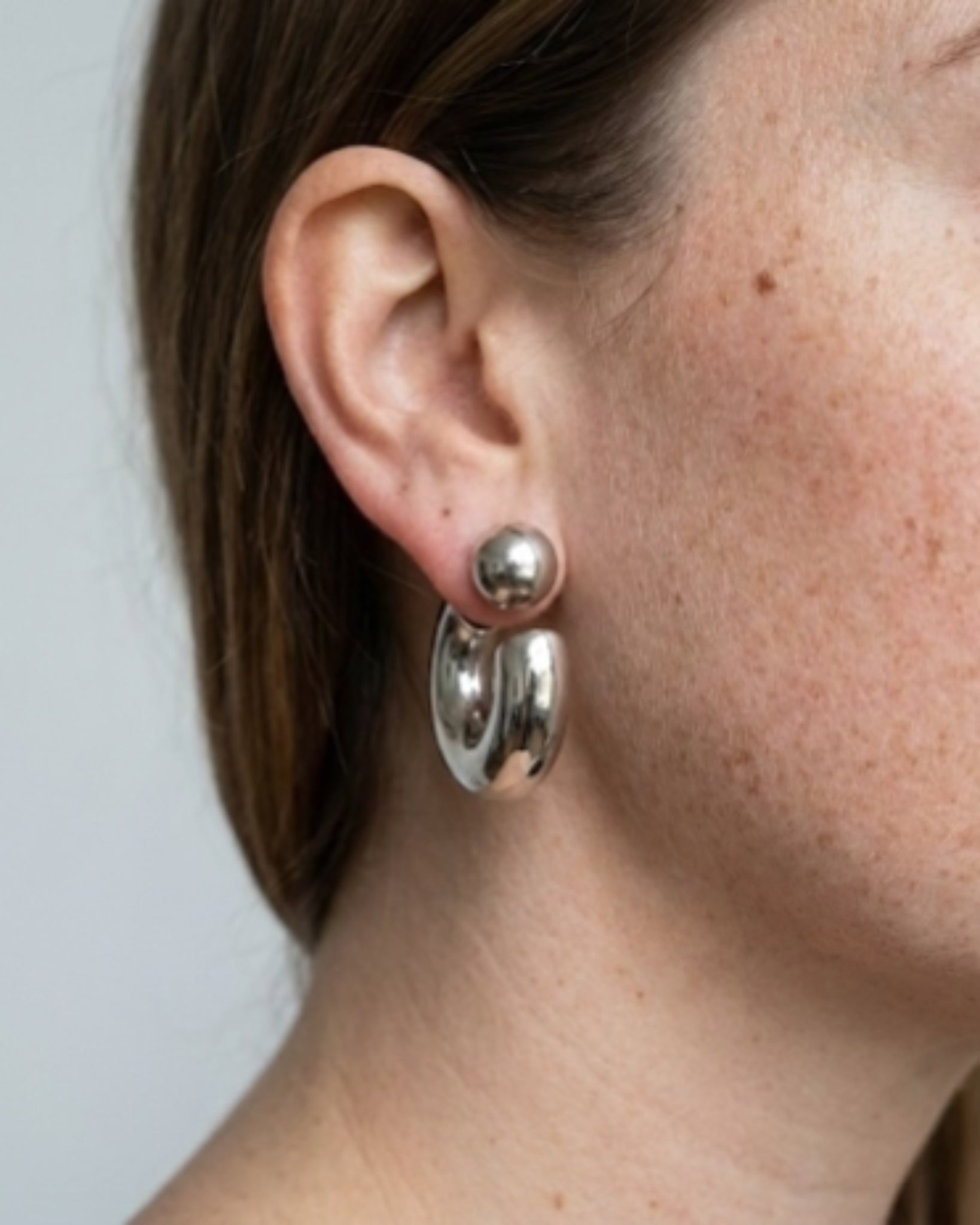 Close-up of a person wearing silver hoop earrings with a neutral background