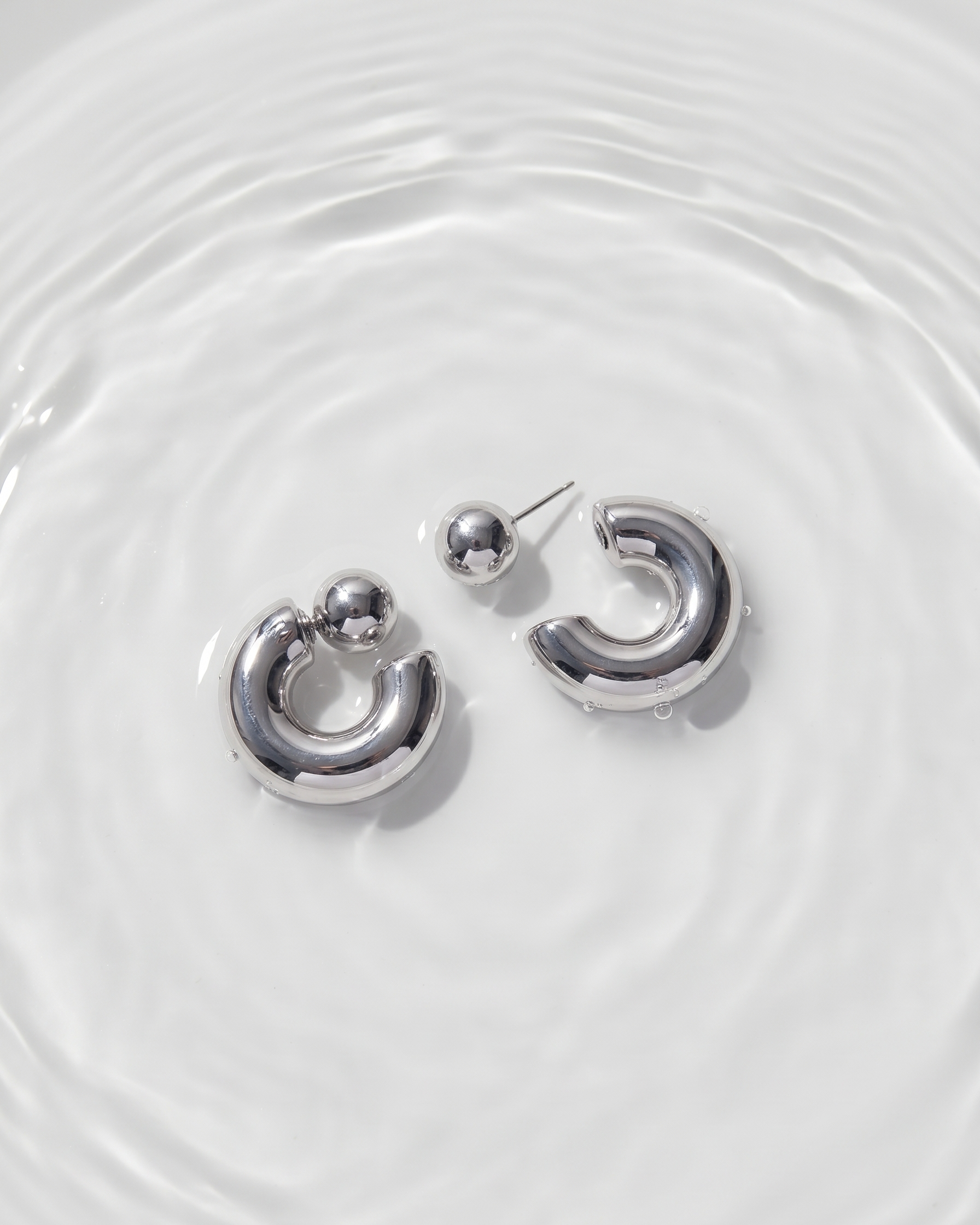 Silver hoop earrings on a white surface with water ripples