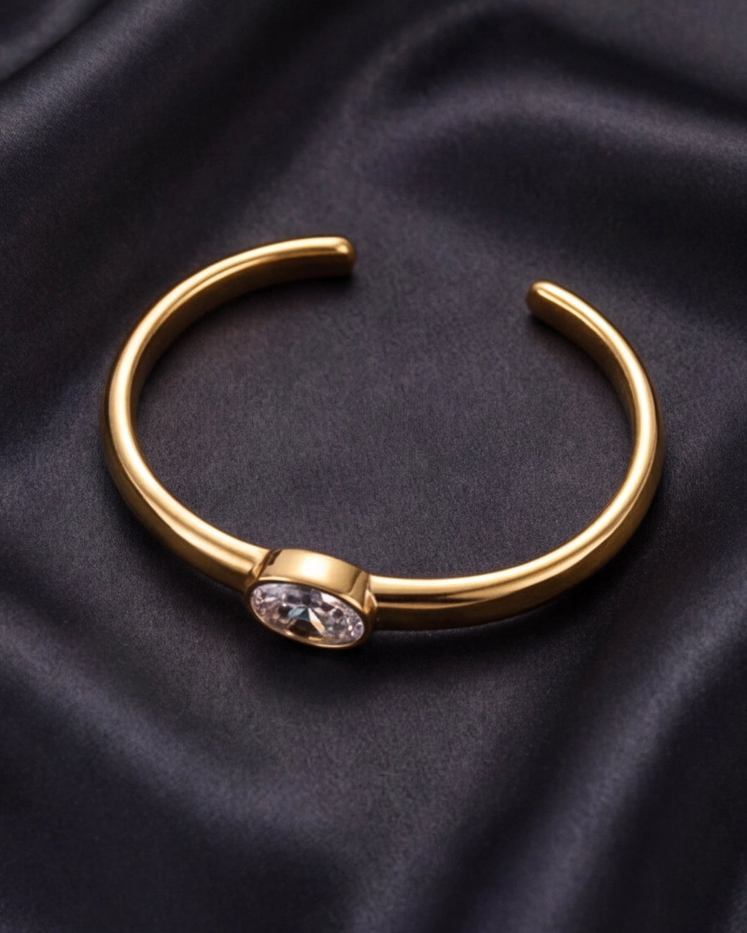 Gold bracelet with a central gemstone on a dark fabric background