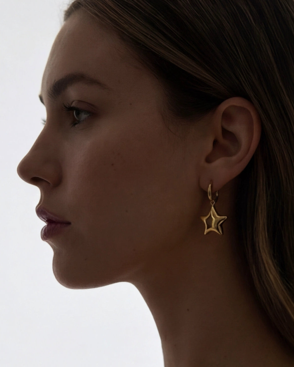 Close-up of a woman wearing a star-shaped earring against a neutral background