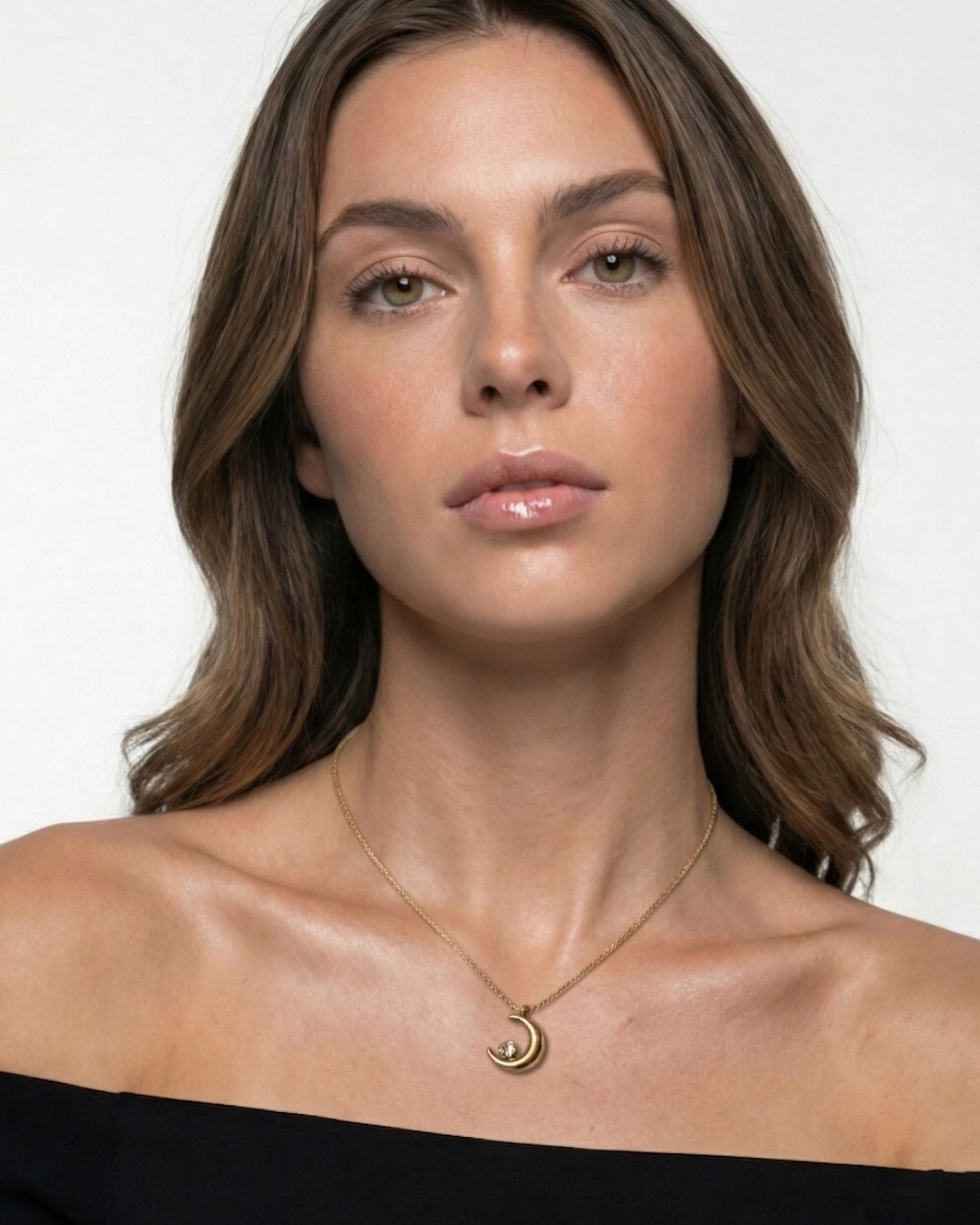 Woman wearing a necklace with a moon pendant against a plain background