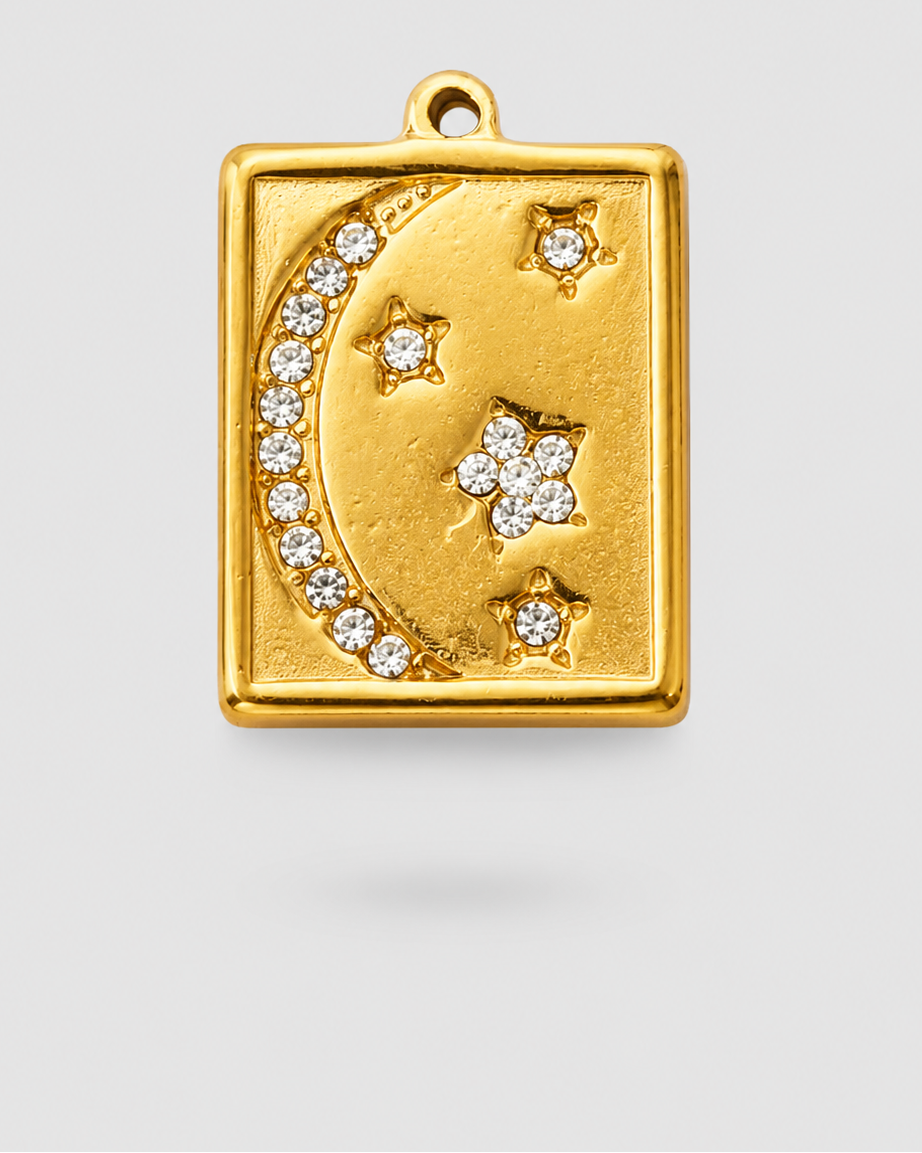 A gold-toned rectangular pendant charm featuring a crescent moon and stars, embellished with small clear stones, shown on a light gray background.