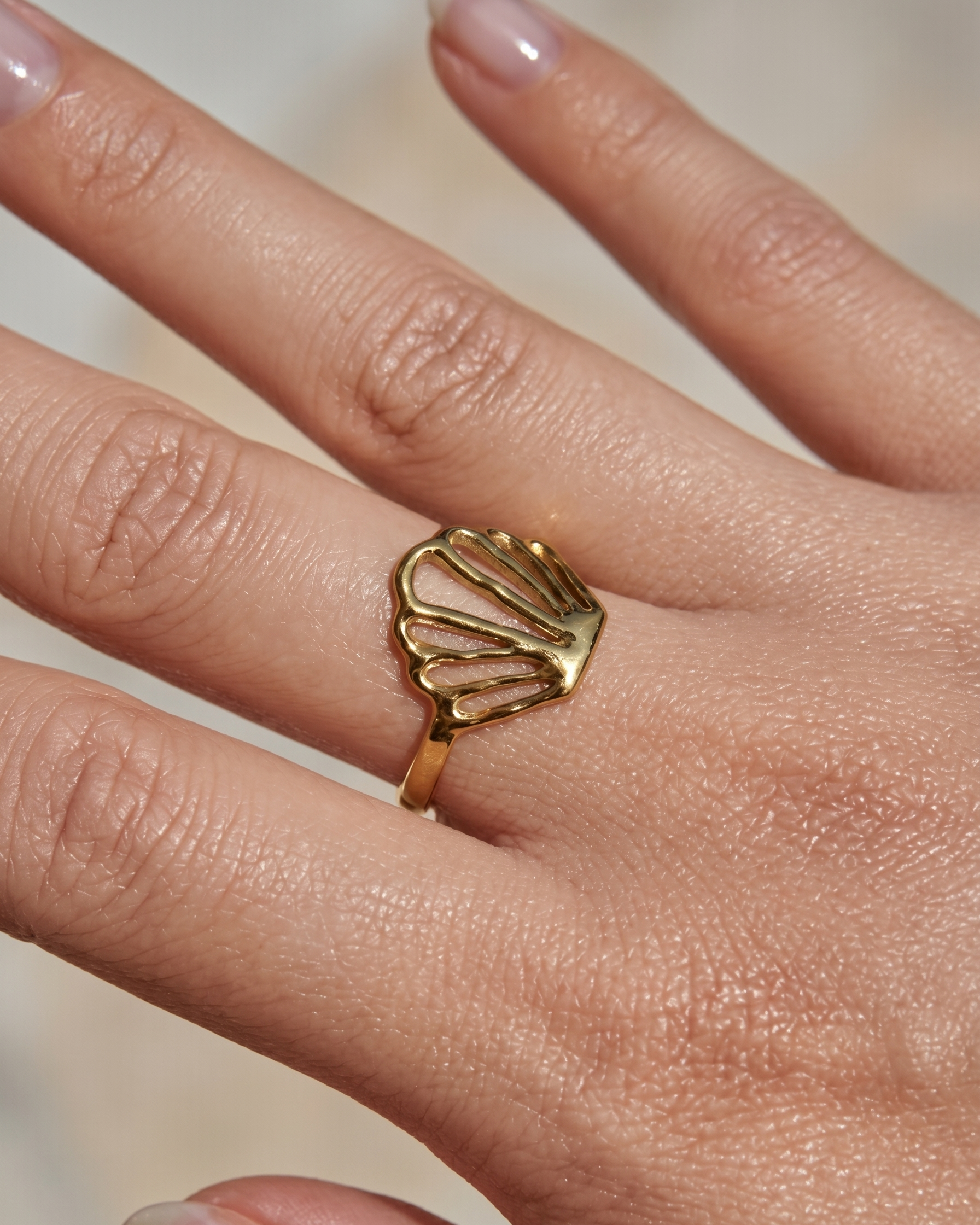 Gold shell-shaped ring on a finger with a blurred background