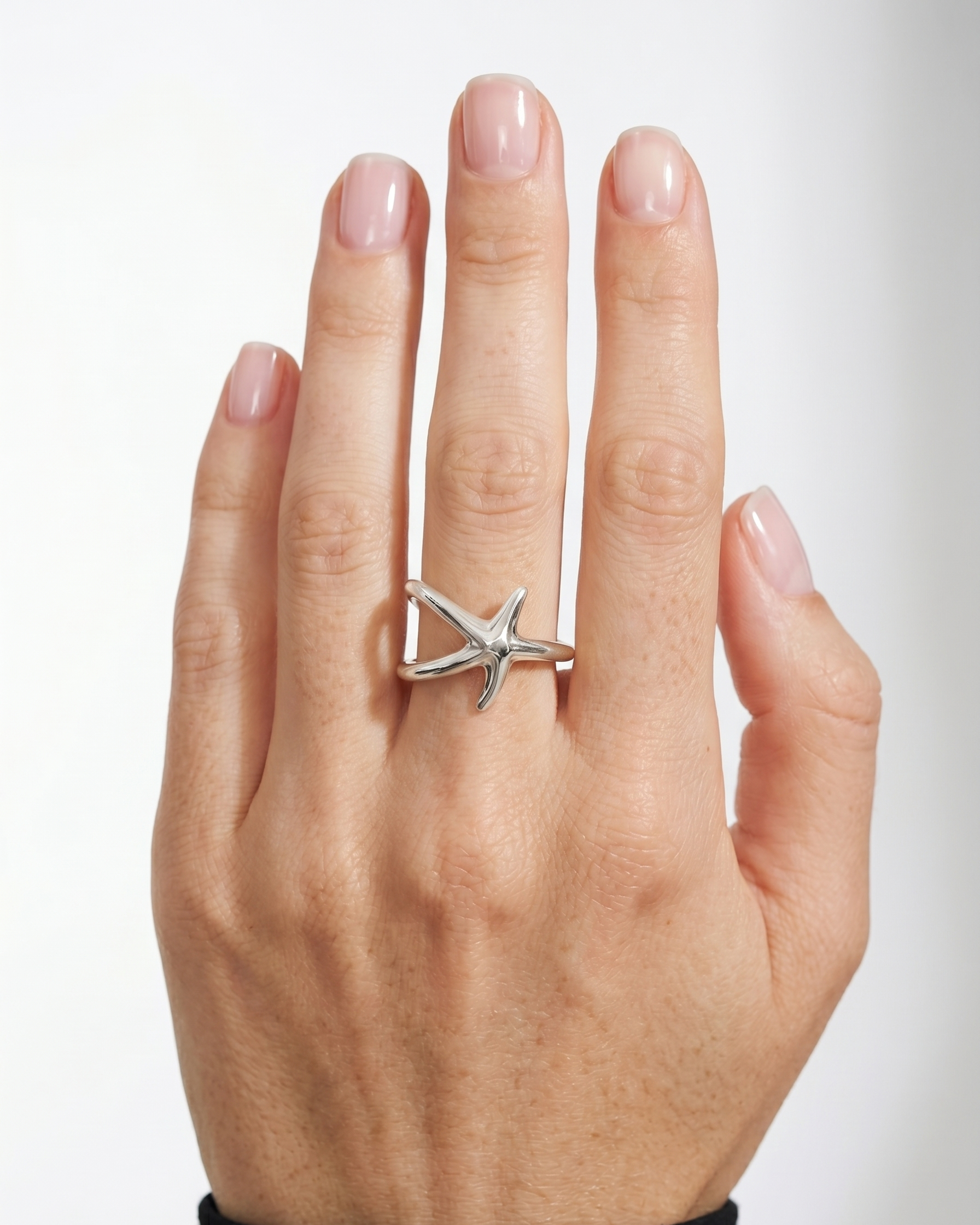 Hand wearing a silver starfish ring on a white background