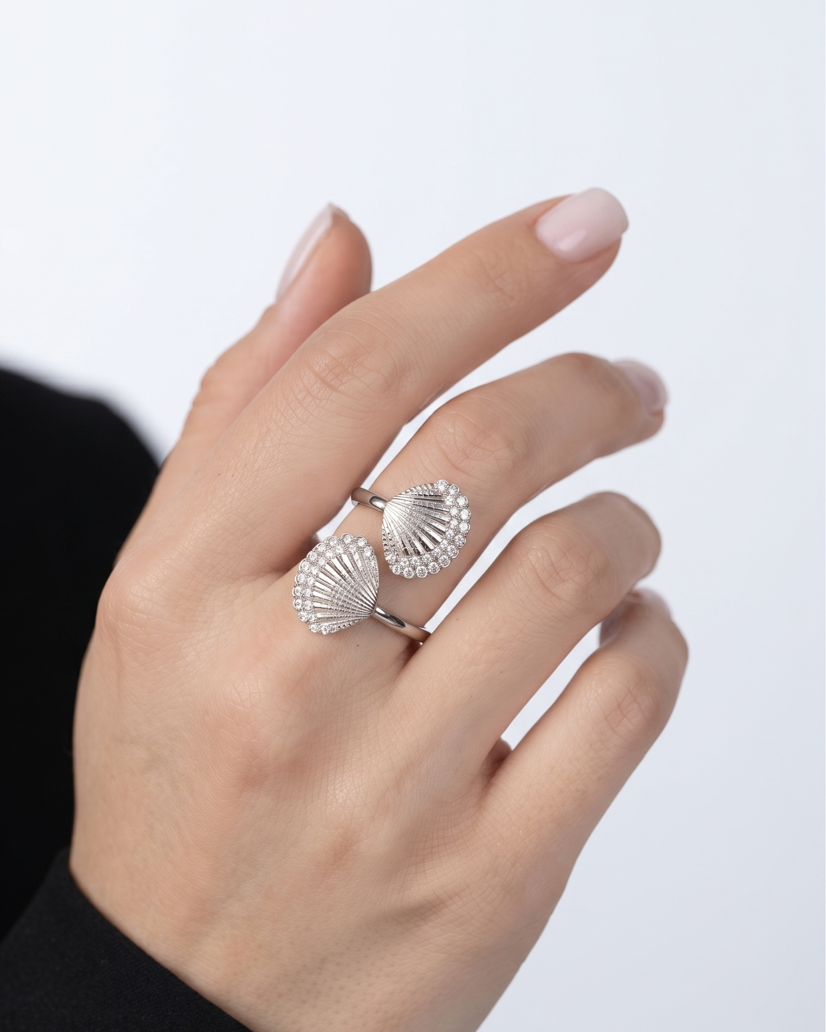 A close-up of a hand wearing two silver seashell-shaped rings, set against a clean white background.