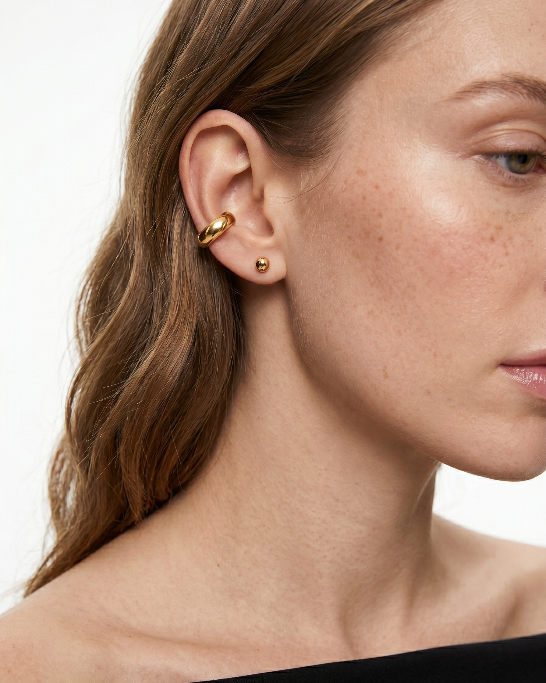 Close-up of a woman wearing gold earrings with a plain background