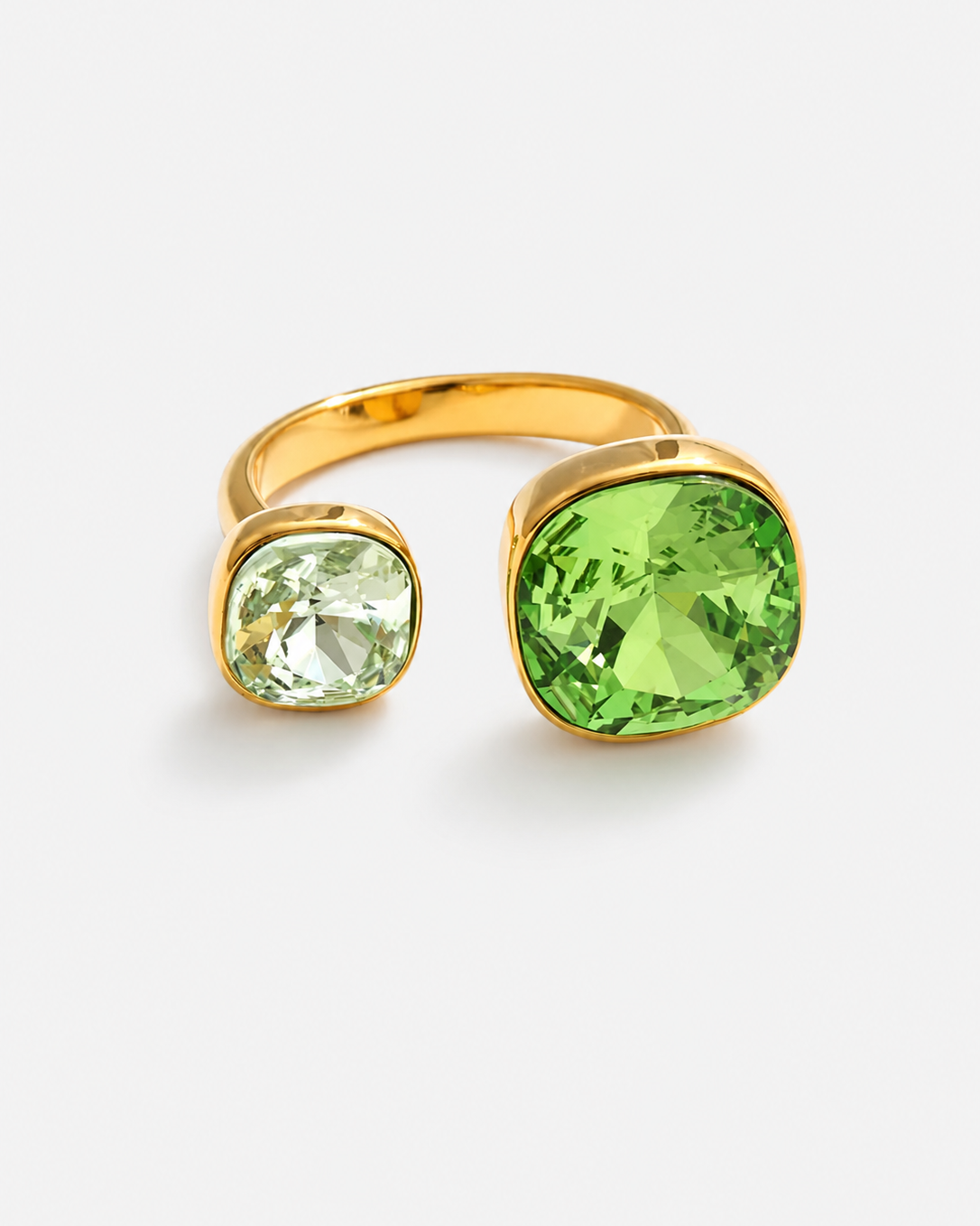 A gold-toned ring with two cushion-cut gemstones, one large light green and one smaller pale green, set against a light gray background.