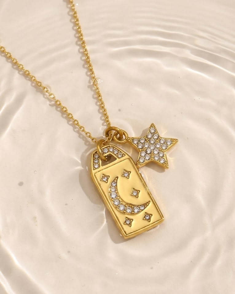Gold necklace with star and rectangular pendant on a textured beige surface