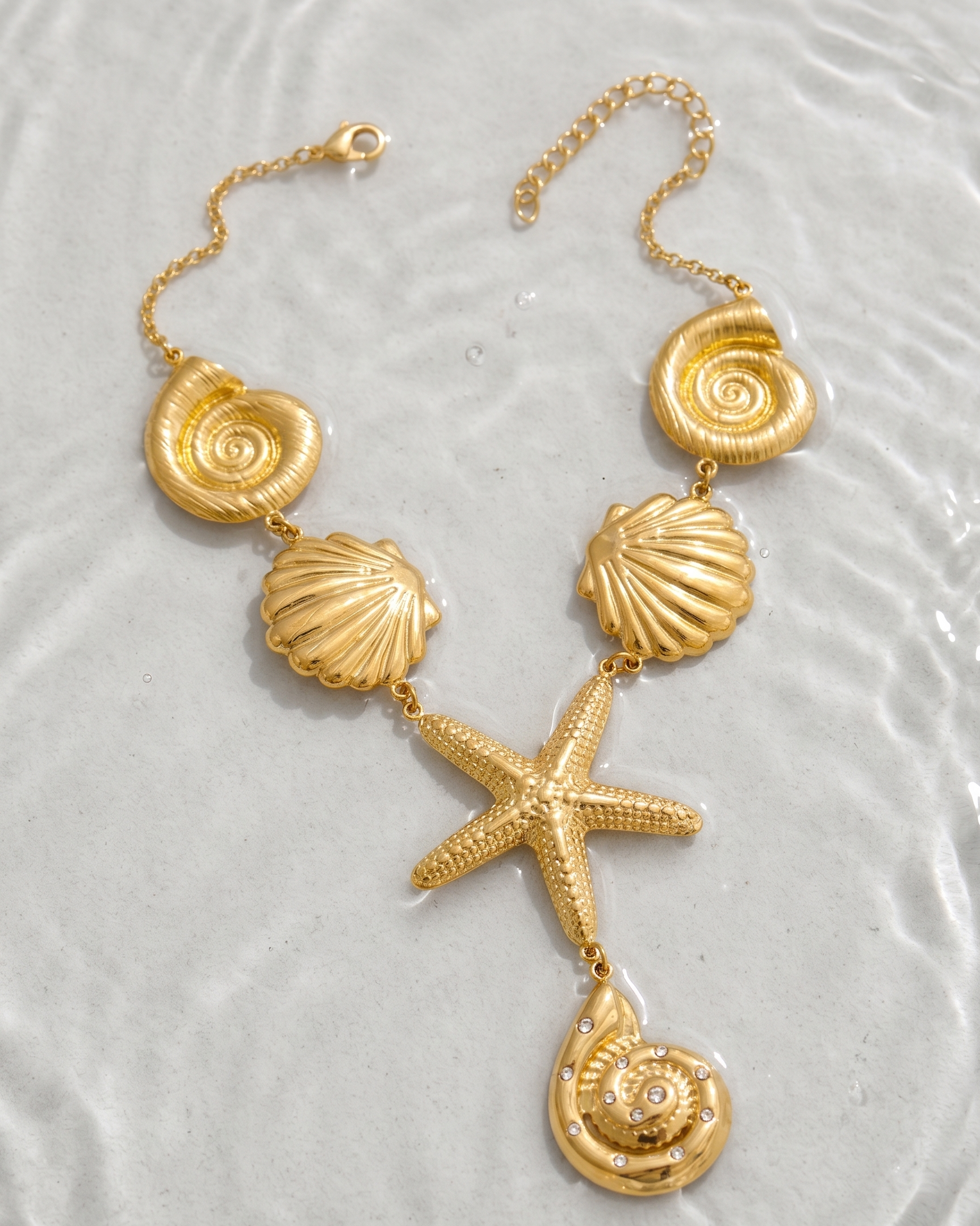 Gold necklace with shell and starfish pendants on a textured white surface