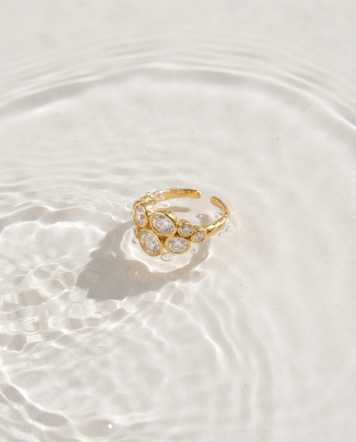 A gold ring with marquise-cut clear gemstones, resting on a surface of rippling water.
