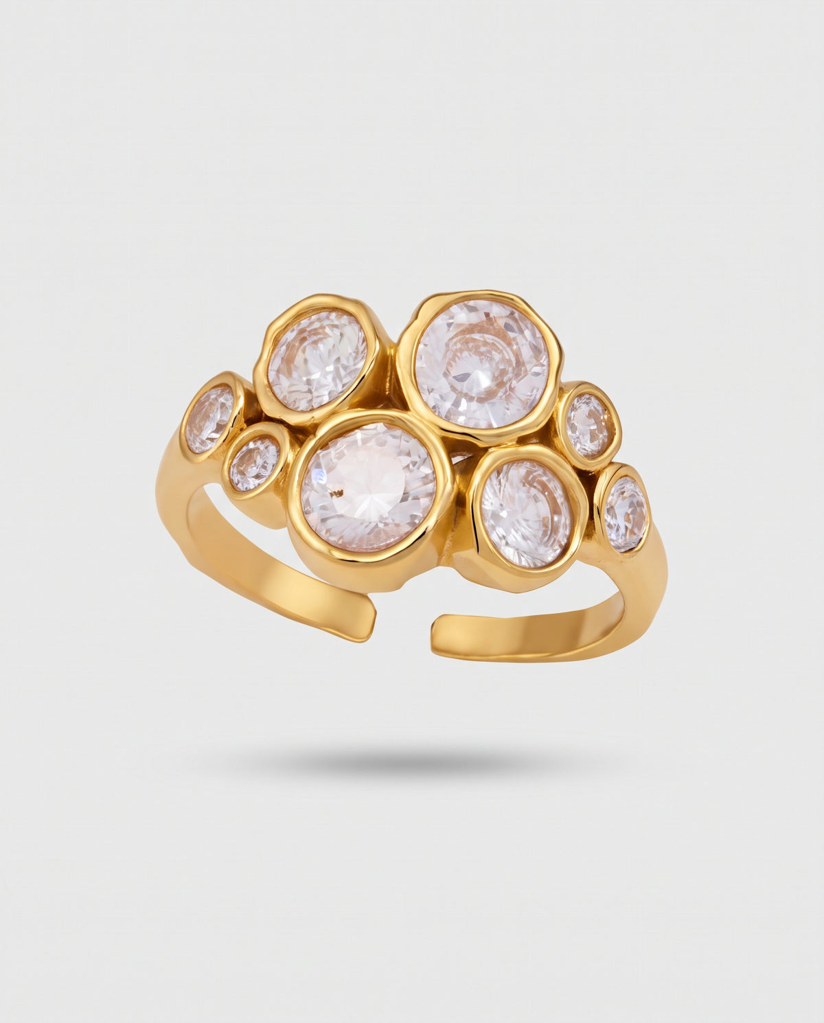 A gold adjustable ring featuring a cluster of bezel-set clear gemstones in irregular circular shapes, shown on a light gray background.