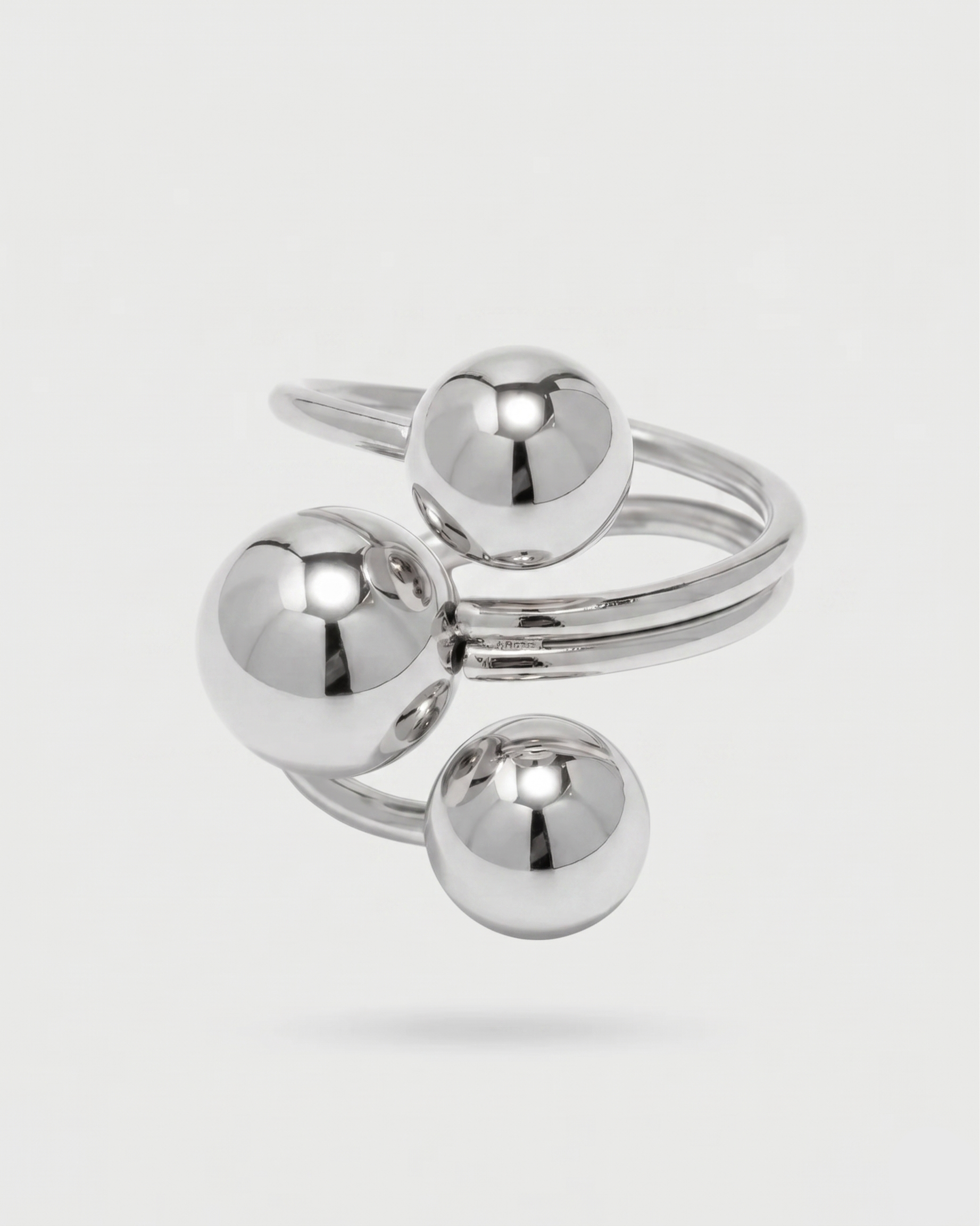 Silver ring with three spherical components on a light gray background