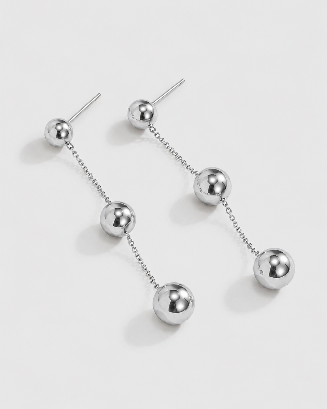 A pair of silver-toned dangle earrings with a series of polished ball beads connected by short chains, shown on a light gray background.
