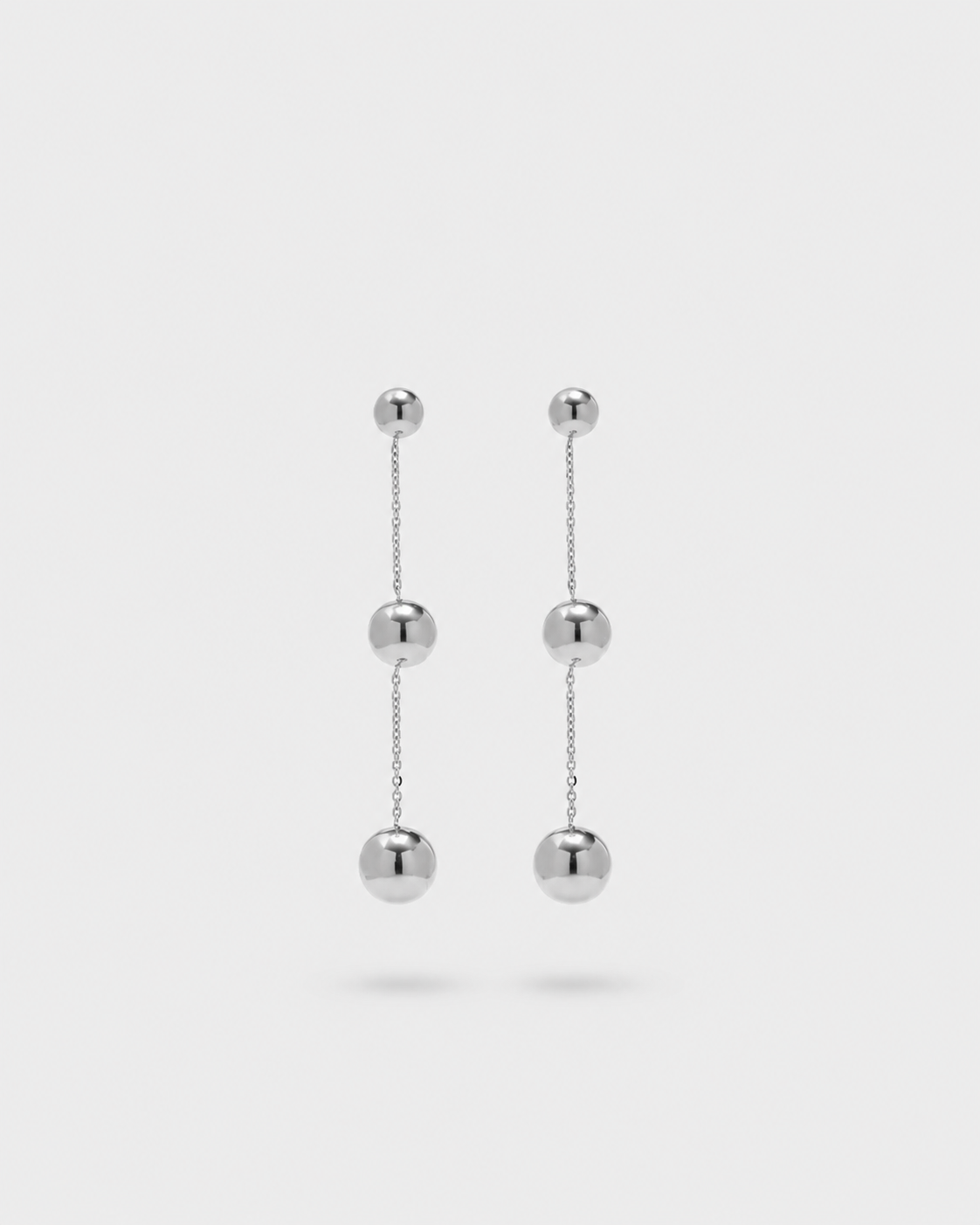A pair of silver drop earrings with three spherical beads connected by delicate chains, shown against a light gray background.