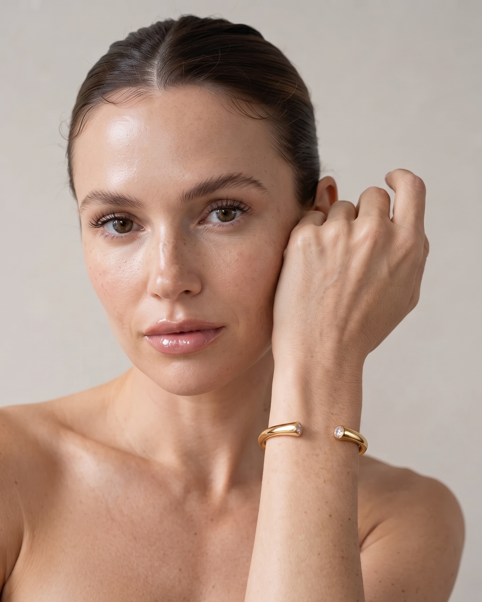 A close-up of a woman wearing a minimalist gold cuff bracelet on her wrist, set against a soft beige background.