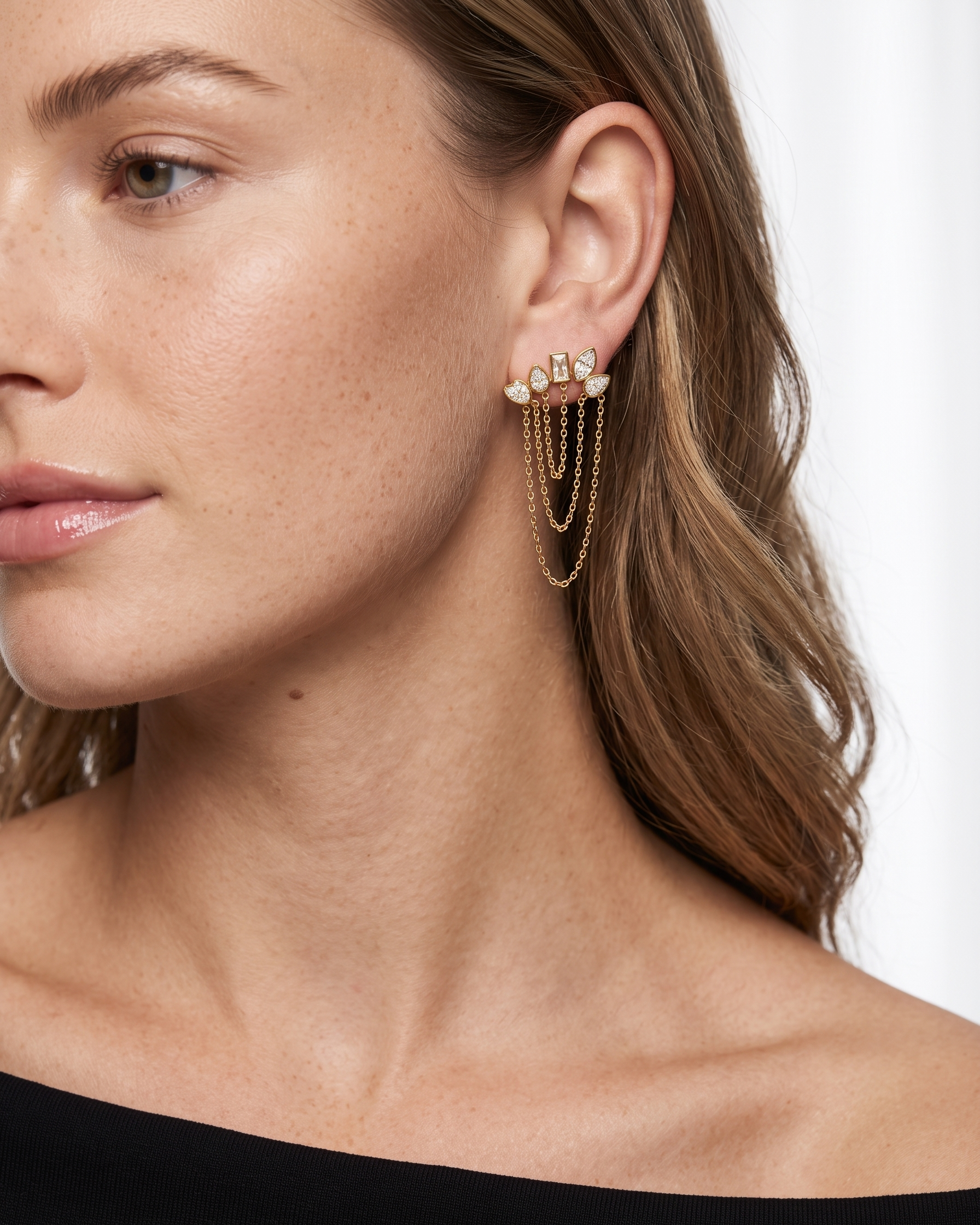 Close-up of a woman wearing gold chain earrings with small stones on a white background