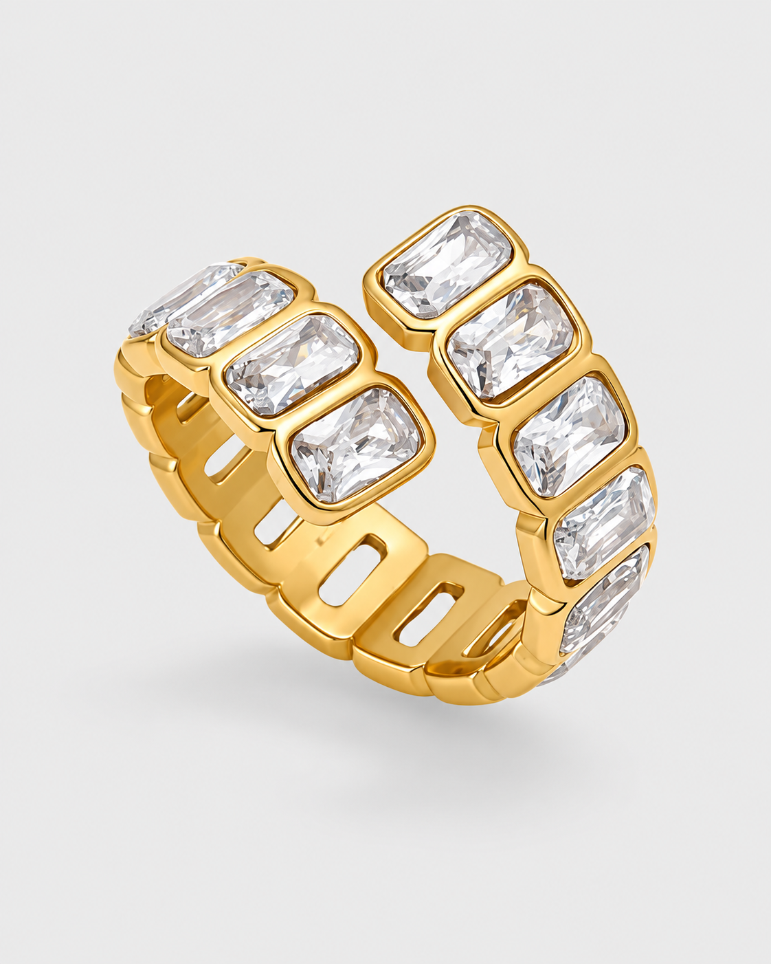 A gold band ring featuring a series of clear rectangular baguette-cut gemstones set in a split double-band design, shown on a light gray background.