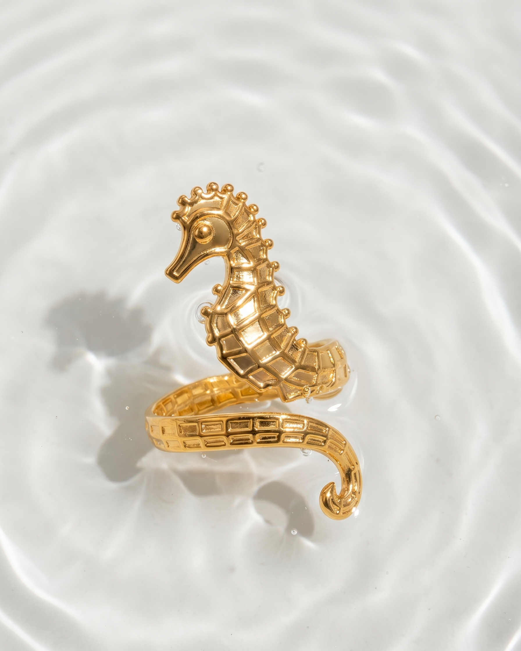 Gold seahorse-shaped ring on a white surface with water ripples