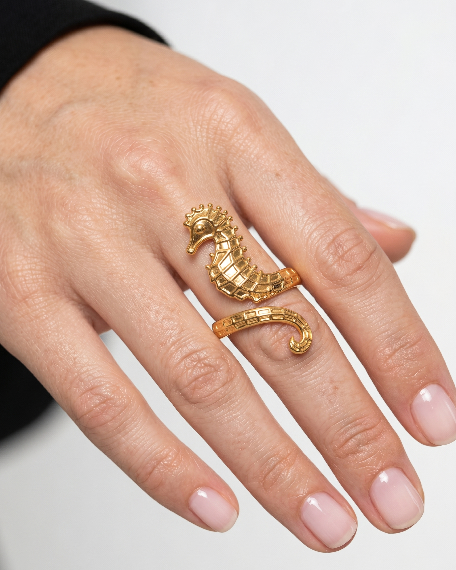 Gold seahorse ring on a person's finger against a neutral background