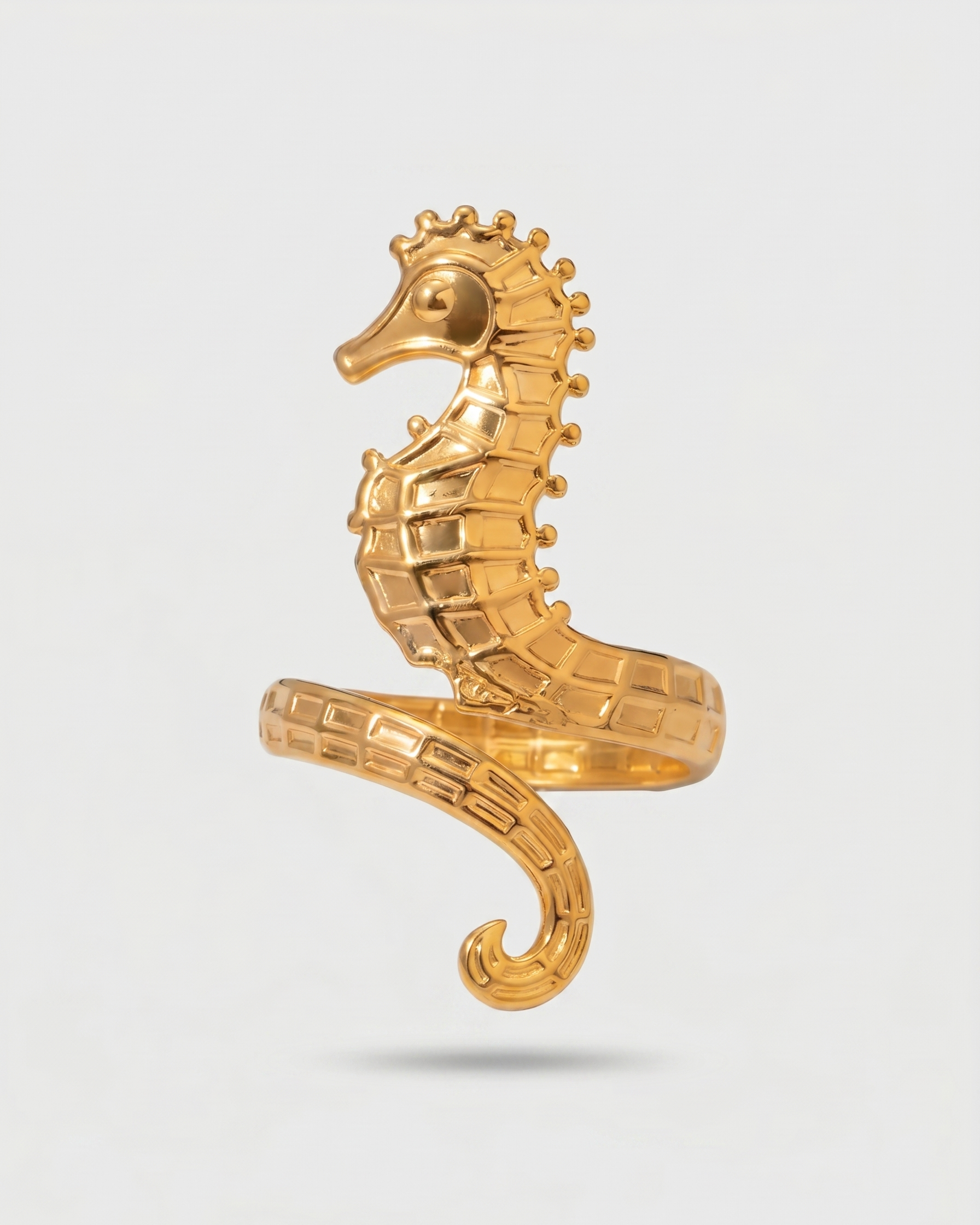 Gold seahorse-shaped ring on a light gray background